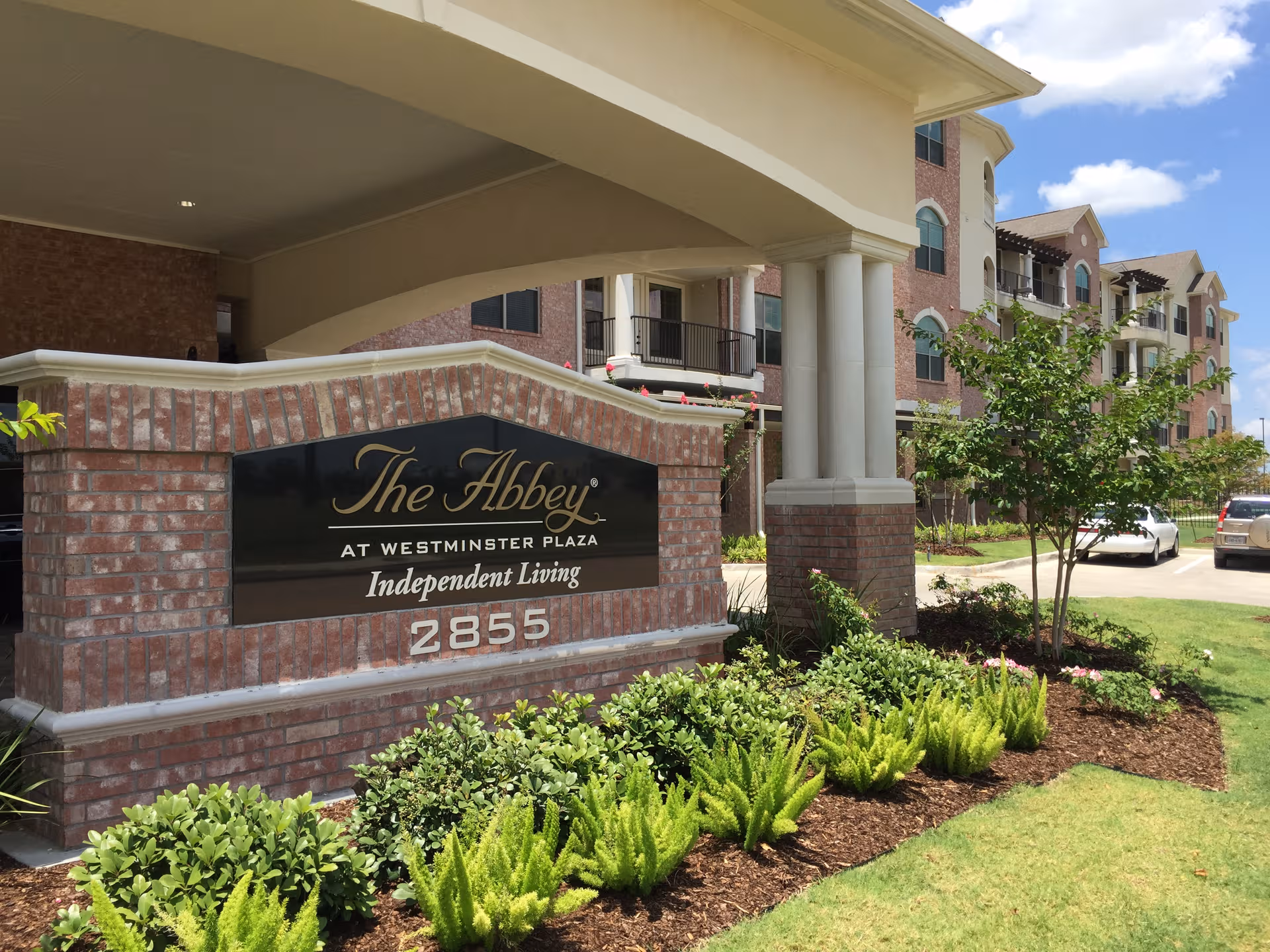 Exterior view of The Abbey at Westminster Plaza with brick signage and landscaping.