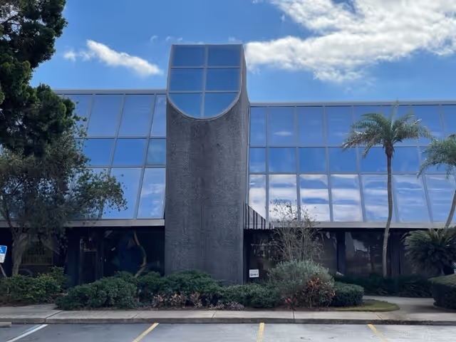 This exterior shows a modern glass-front facility with palm trees and manicured landscaping.