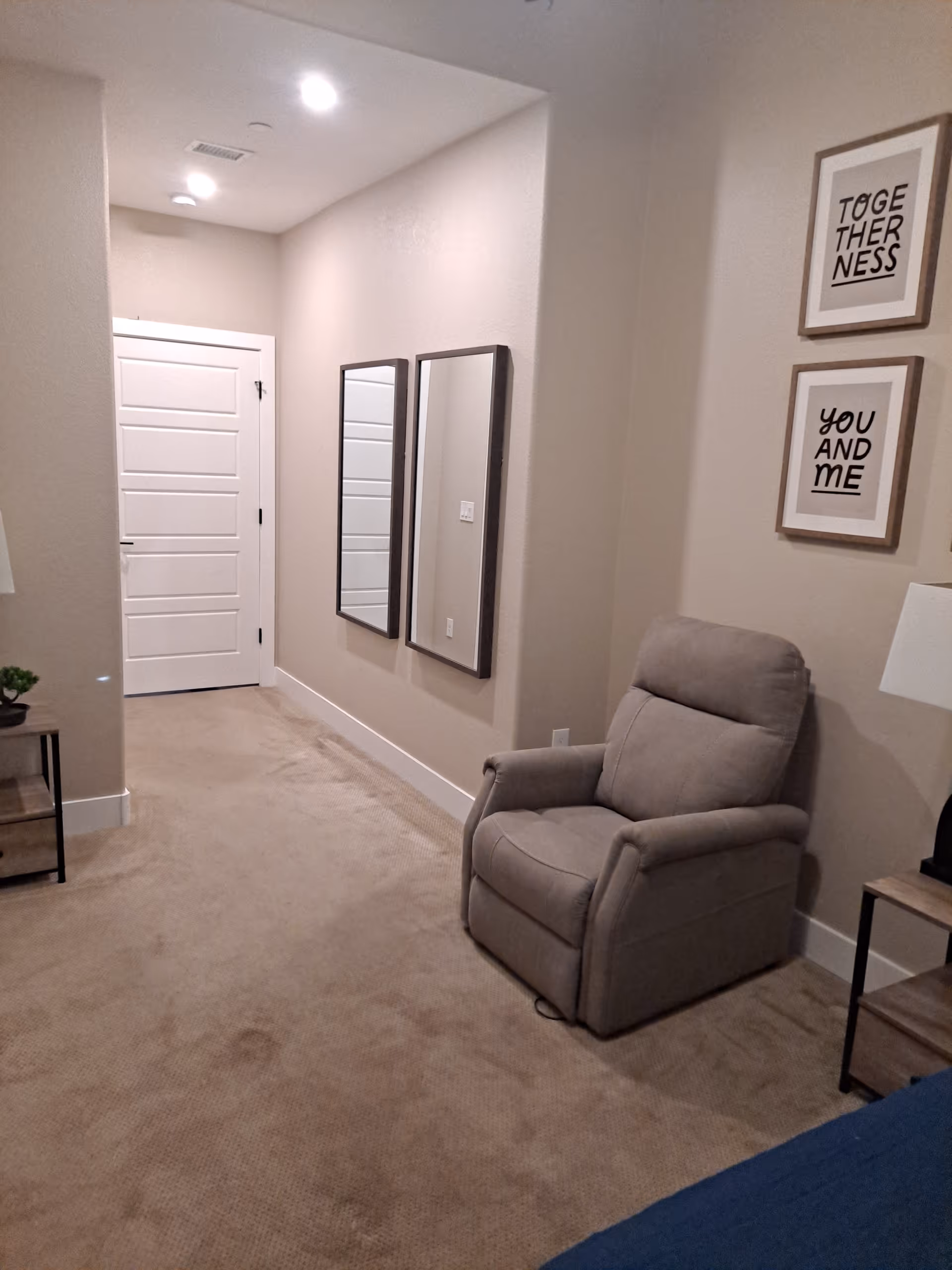 Hallway scene in a senior living facility with a beige recliner and framed wall art.