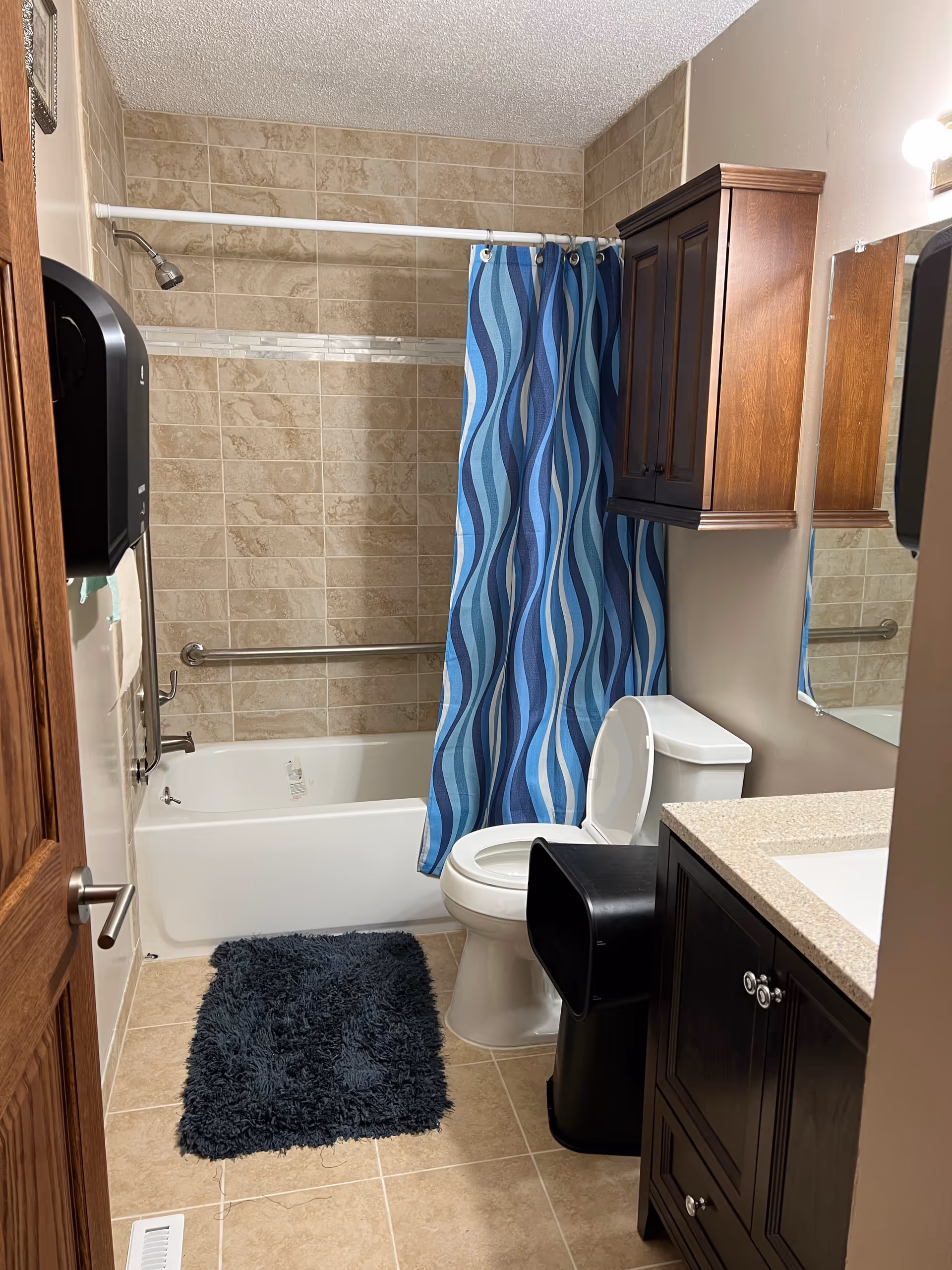 Small bathroom in a senior living facility with bathtub, toilet, sink, and blue curtain.