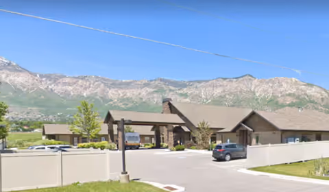 Exterior view of Quail Meadow Assisted Living with driveway, parked cars, and mountains in the background.