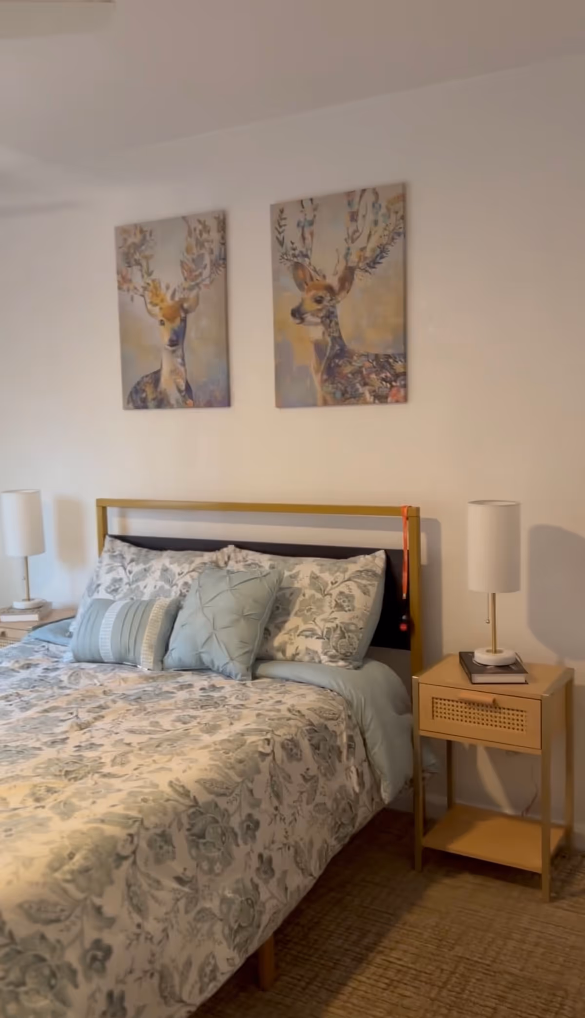 Bright bedroom with floral bedding, two nightstands, lamps, and deer artwork above bed.