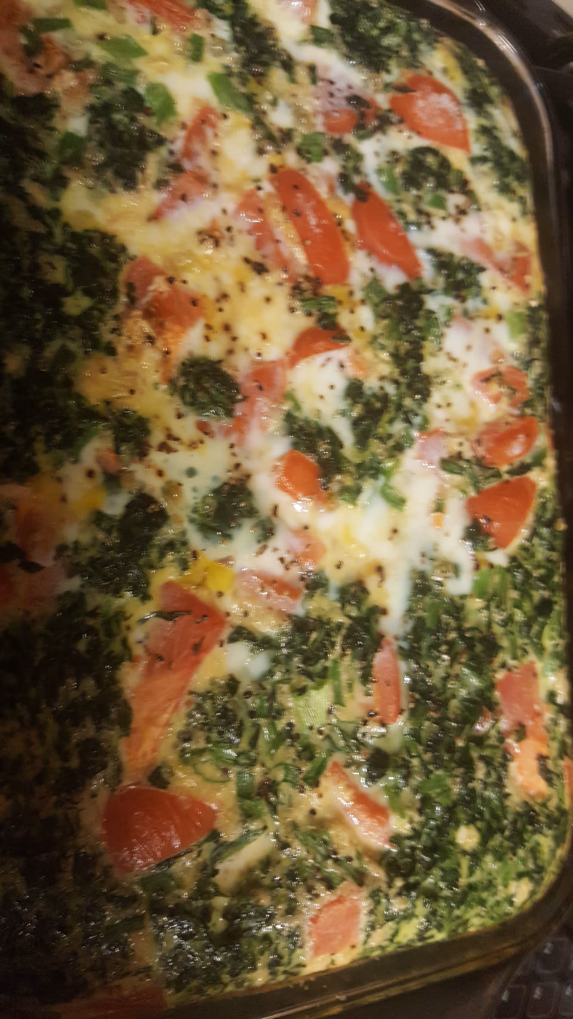 Close-up of a baked frittata with greens, tomatoes, and melted cheese in a pan.
