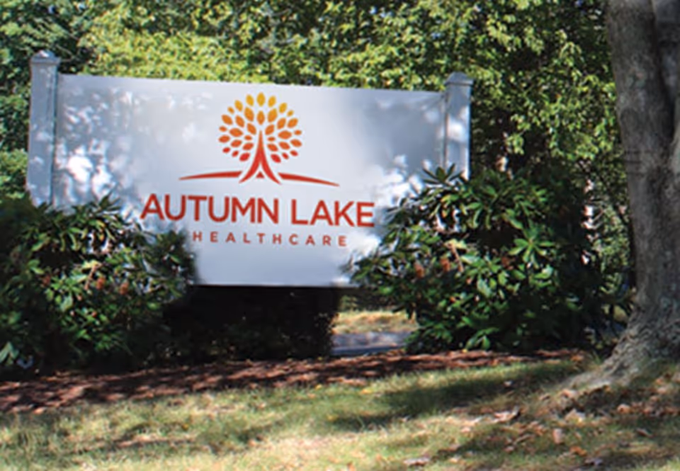 Outdoor sign reading Autumn Lake Healthcare stands among trees and shrubs.