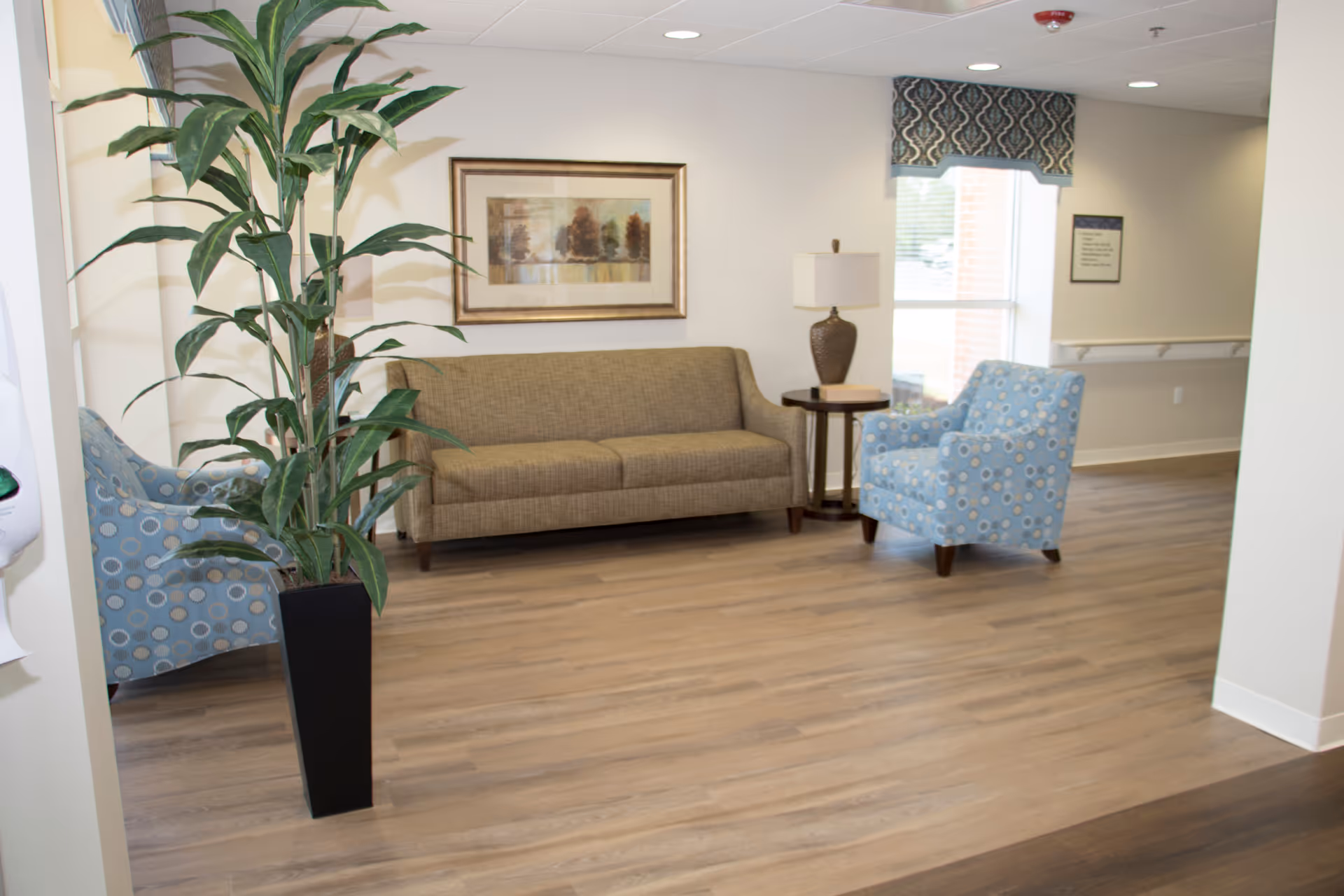 A waiting lounge at Magnolia Manor of Marion County with sofa, blue chairs, plant, and lamp.