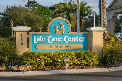 Entrance sign for Life Care Center of Palm Bay with landscaped shrubs.