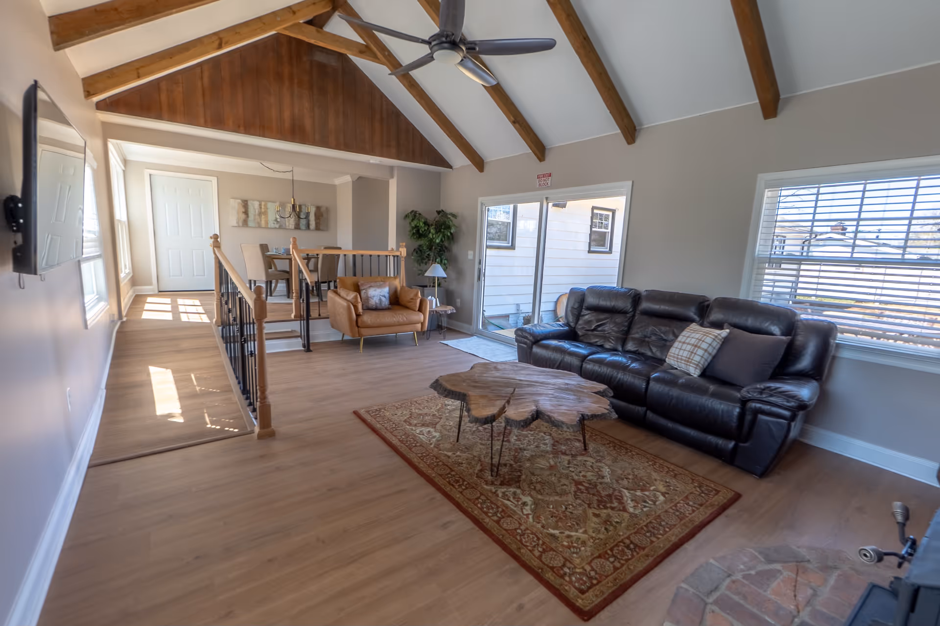 Bright, open living room with leather sofa, rug, coffee table, and wooden ceiling beams.