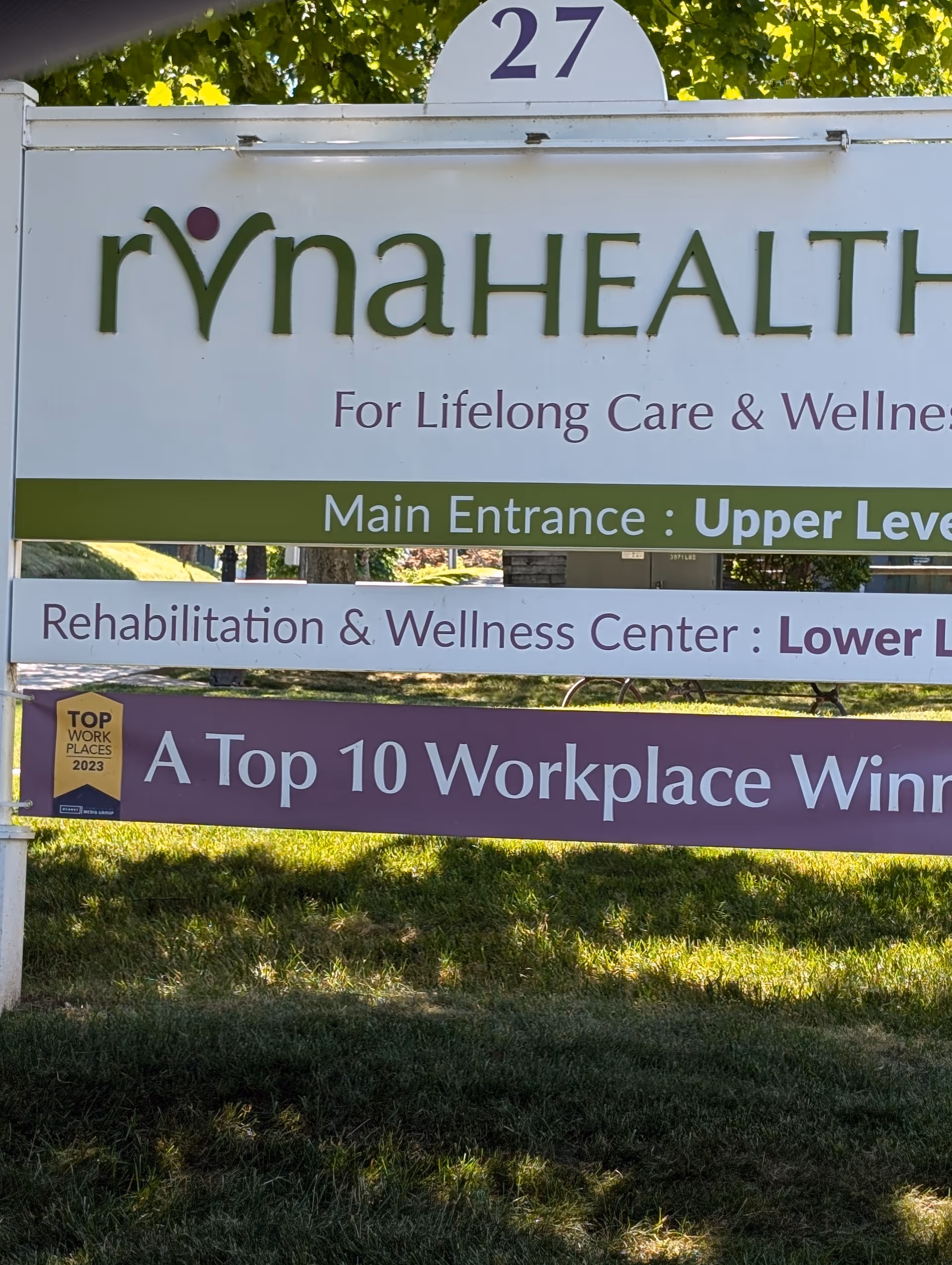 Outdoor sign for RVNAhealth with main entrance directions and wellness banners on a grassy front.
