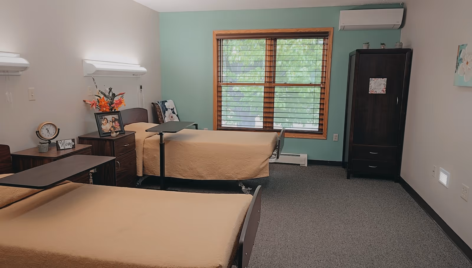 Two beige hospital beds with overbed tables in a bright shared bedroom.