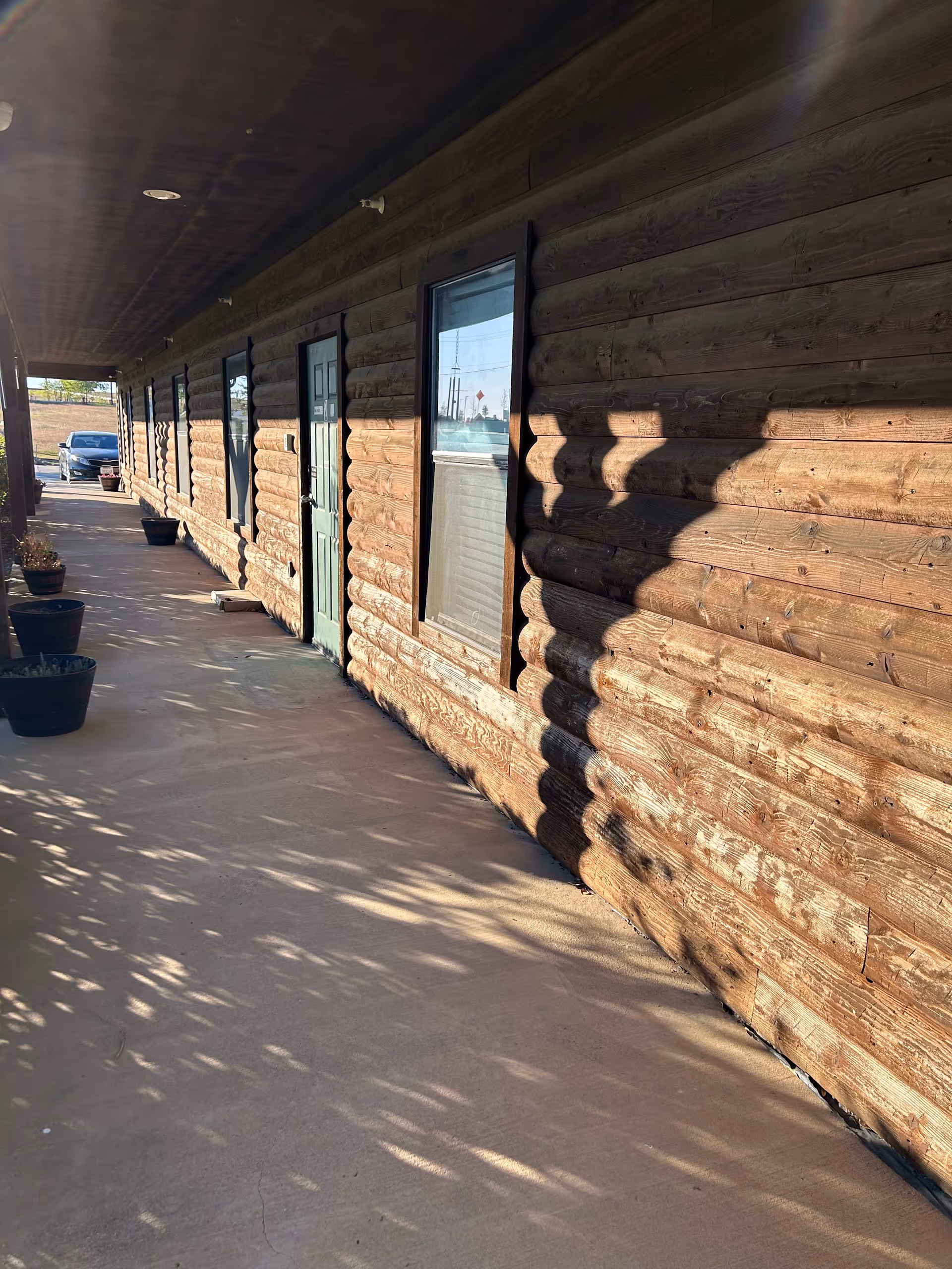 Log-style exterior hallway with doors, windows, and potted plants along a covered walkway.