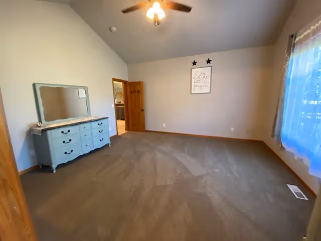 A sparsely furnished bedroom with a dresser, mirror, ceiling fan, and window.