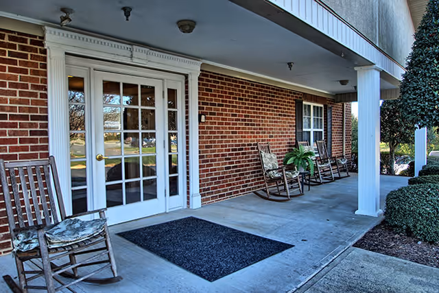 Brick exterior entrance with glass double doors, white trim, and rocking chairs on covered porch.