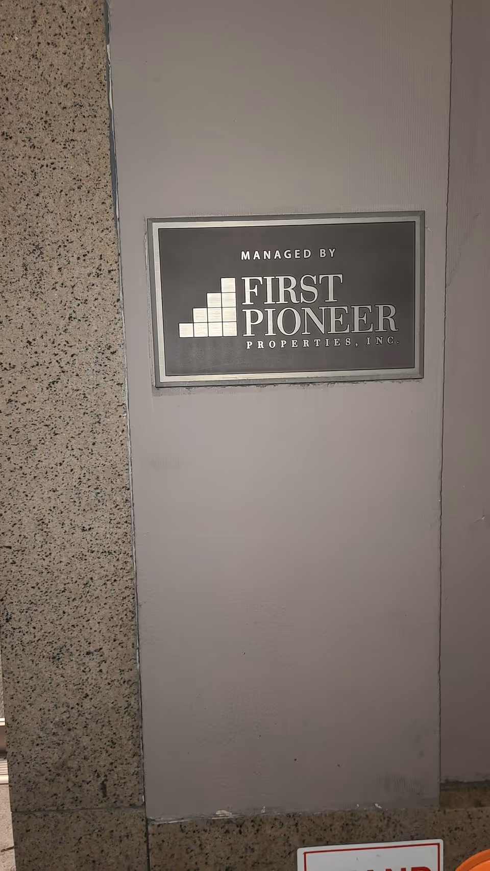 Sign reads 'Managed by First Pioneer Properties, Inc.' mounted on a gray wall.