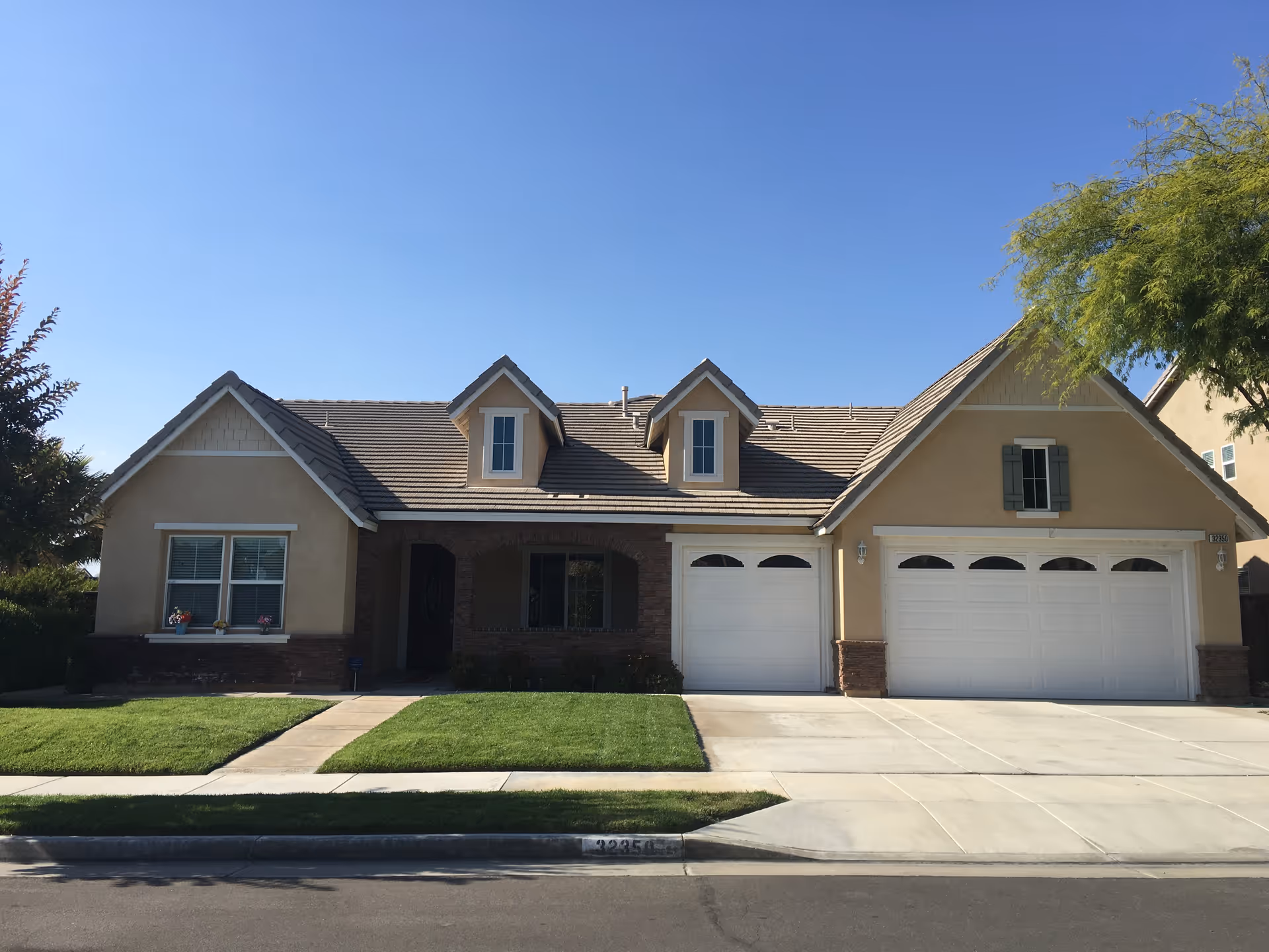 A beige, two-story house-style building with a three-car garage and manicured lawn.