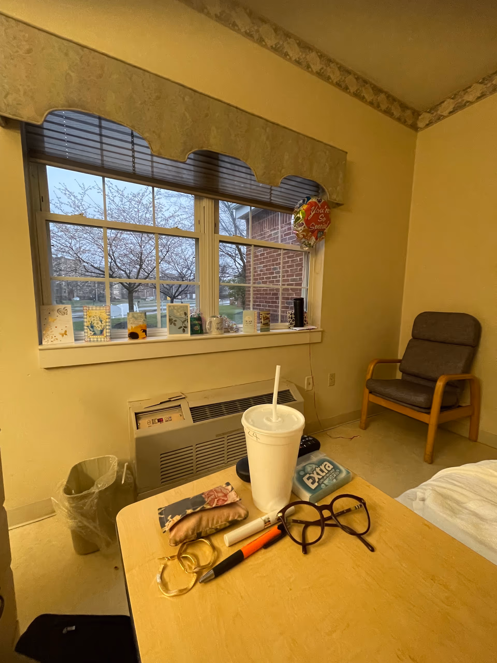 Interior of a senior living room with window, chair, and a cluttered table.