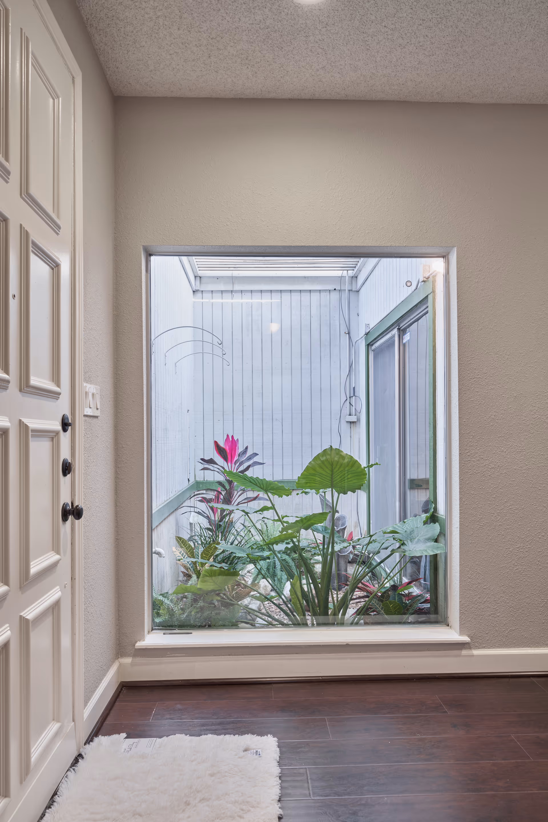 Hallway interior with a window showing tropical plants in a small indoor courtyard.