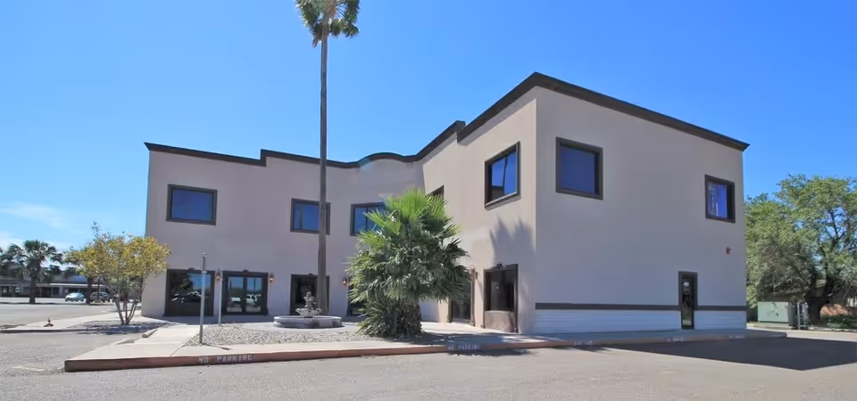 Exterior view of a modern senior care building with palm trees and parking.