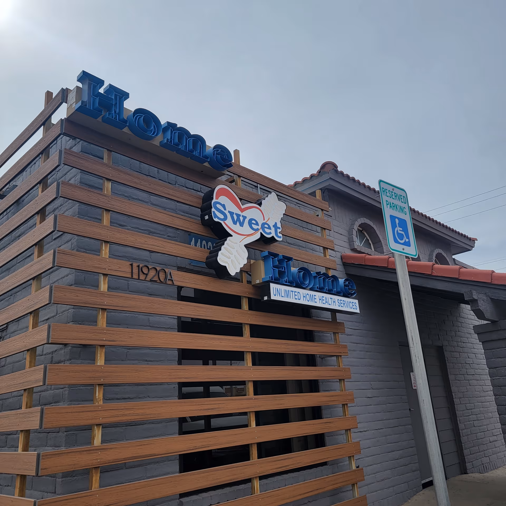 Exterior of a gray brick facility with wooden slats and blue Home Sweet Home sign.
