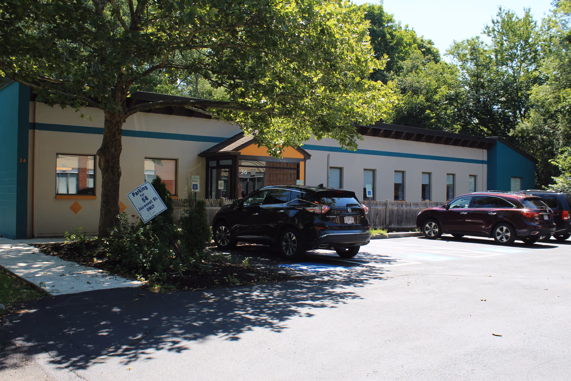 Front view of a single-story Alliance Hospice Care building with parked cars and trees.