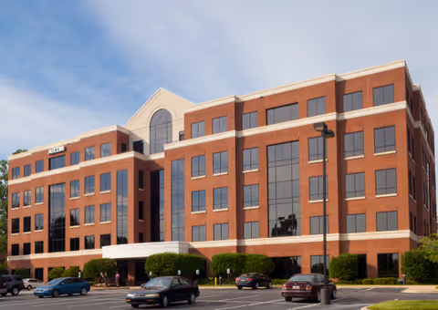 Brick multi-story senior living facility exterior with entrance and parked cars.