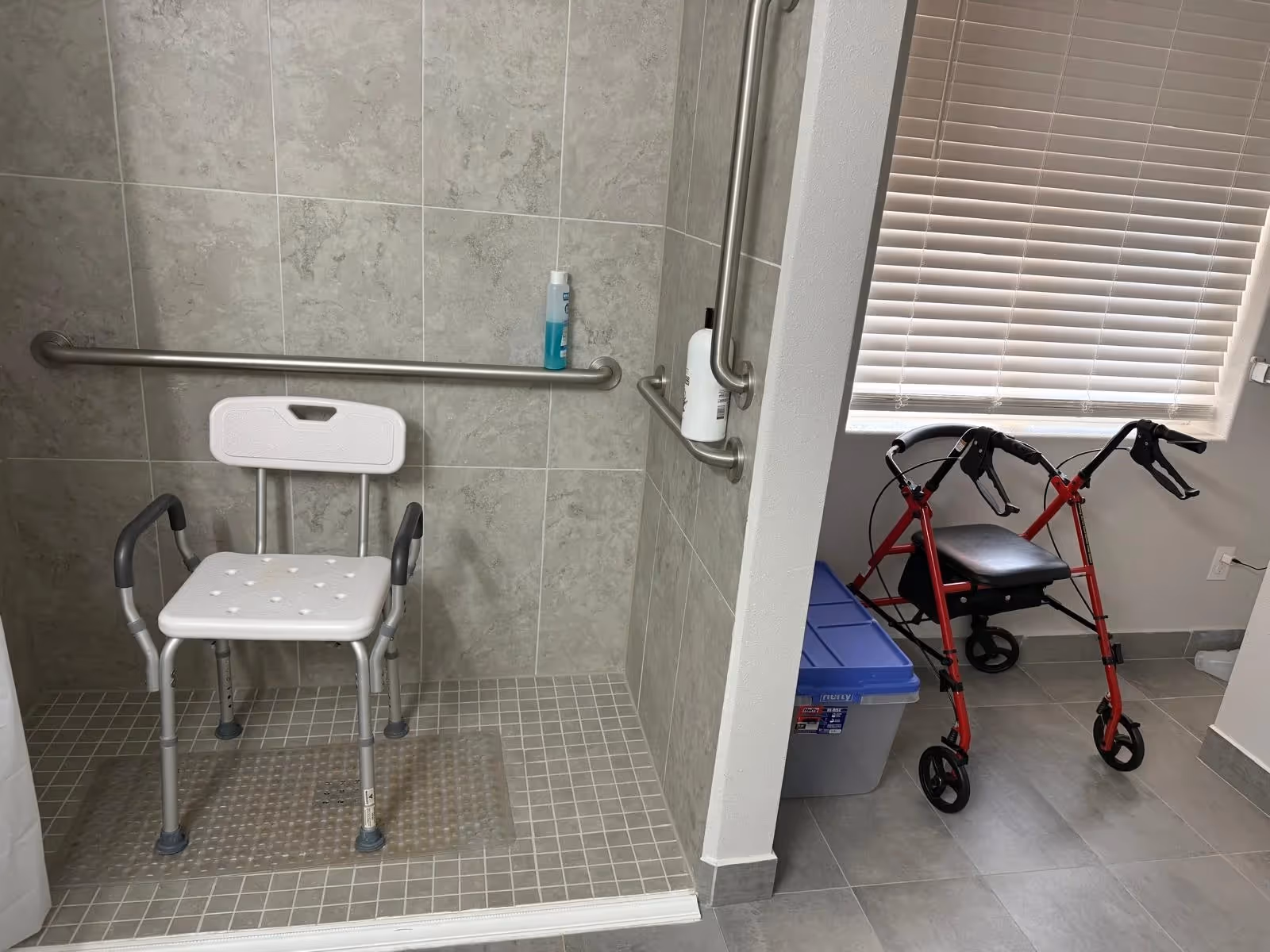 Accessible bathroom with a shower chair, grab bars, and a walker nearby.