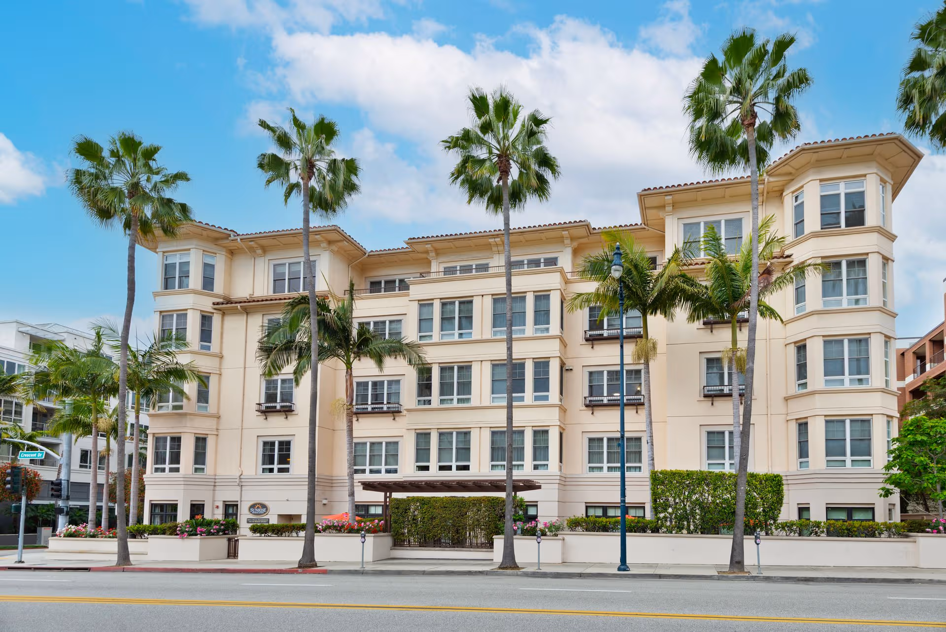 Sunrise of Beverly Hills exterior building with palm trees along a sunny street.