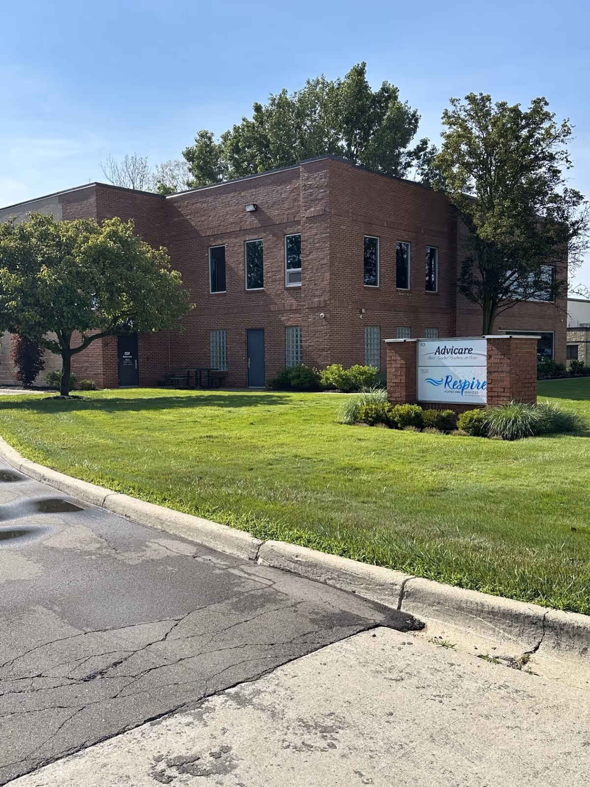 Brick senior living building with a sign and manicured lawn under a blue sky.