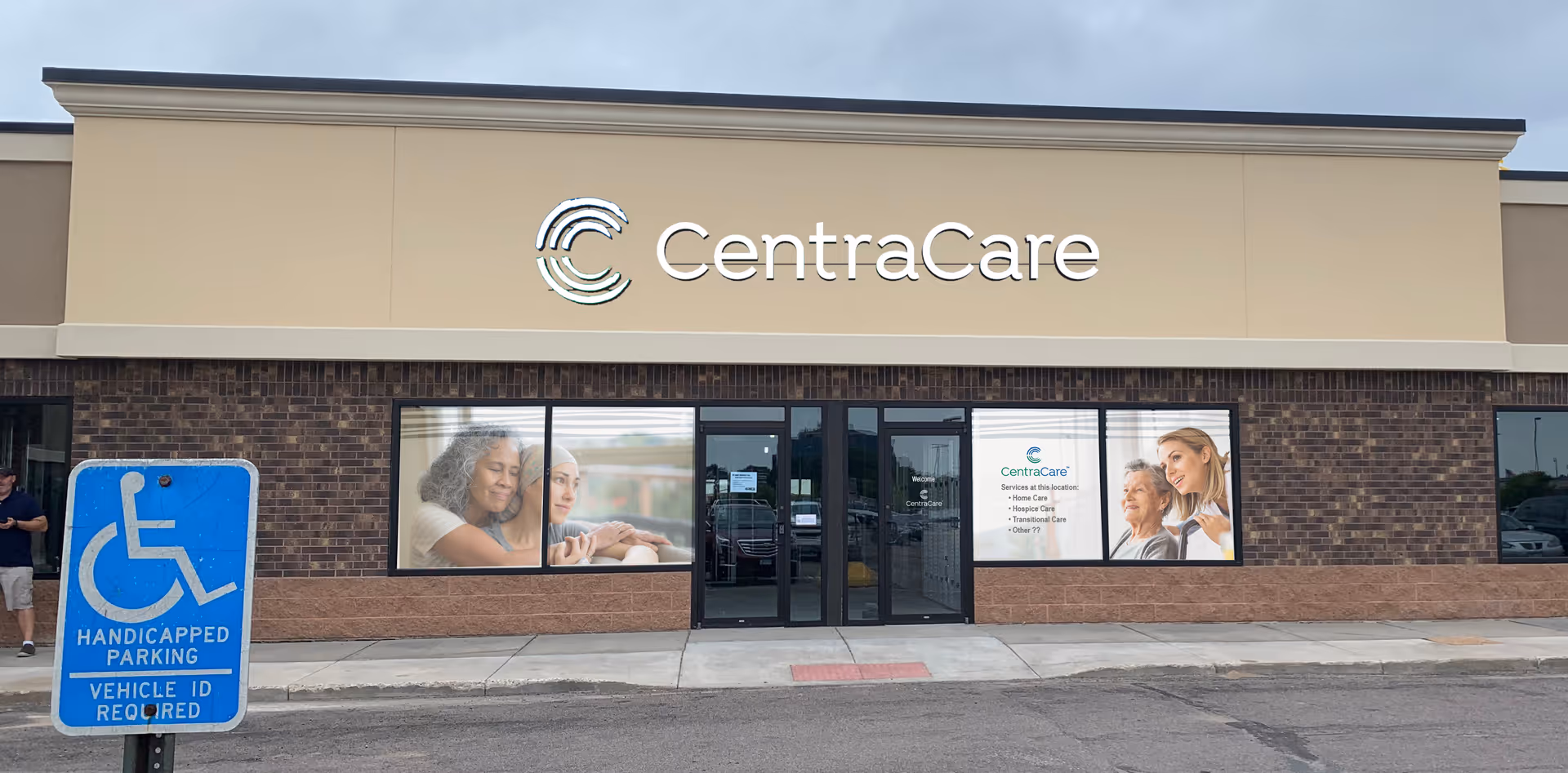 CentraCare facility storefront with beige facade, brick lower wall, glass entrance, and a blue handicap sign.