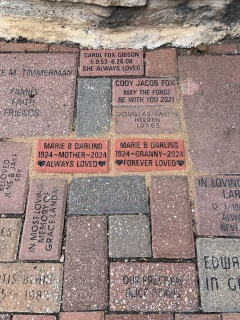 Close-up of engraved memorial bricks on a brick-paved outdoor courtyard walkway.