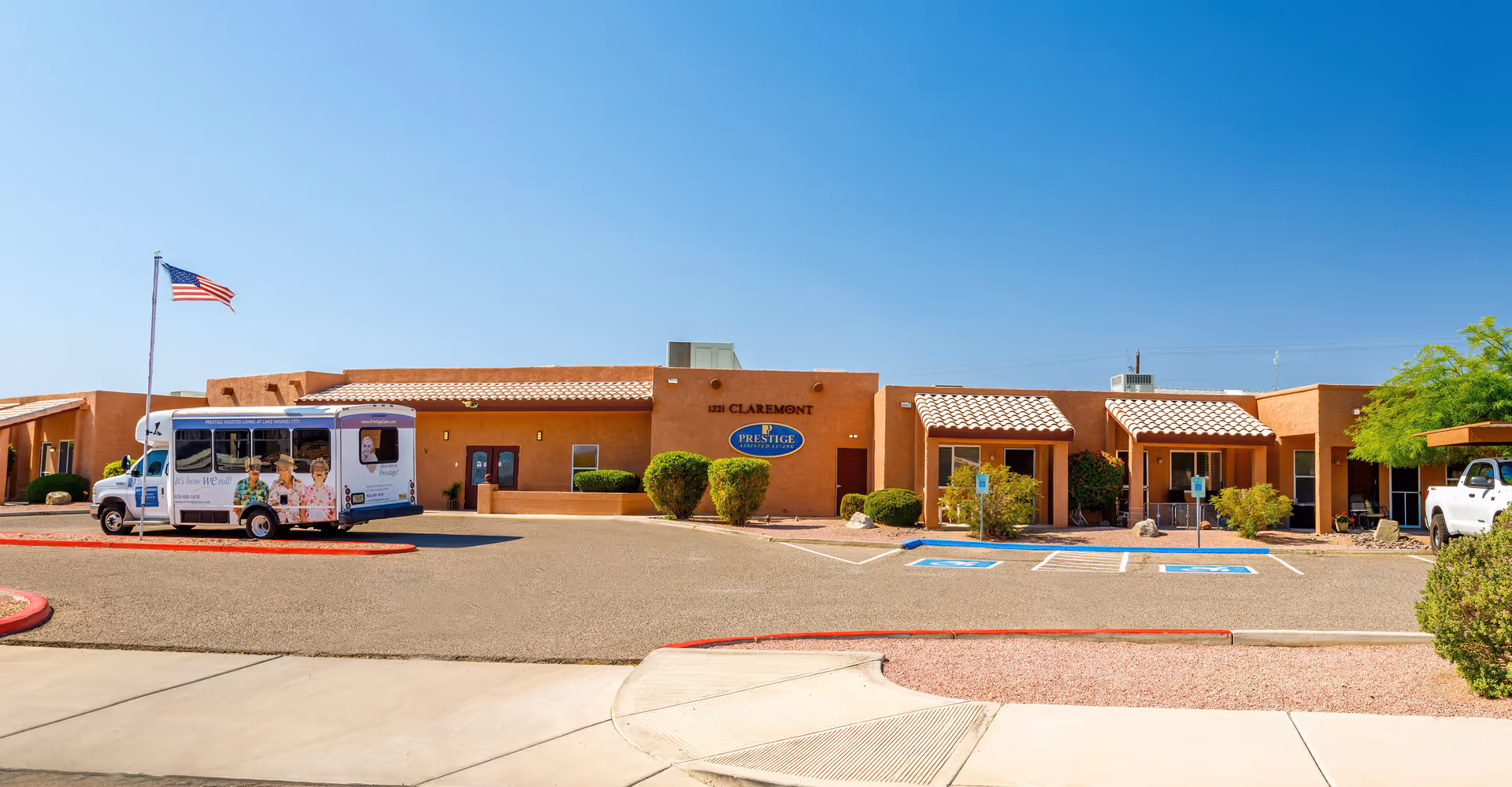 Sunny exterior view of Claremont Assisted Living building with parking lot and a shuttle bus.