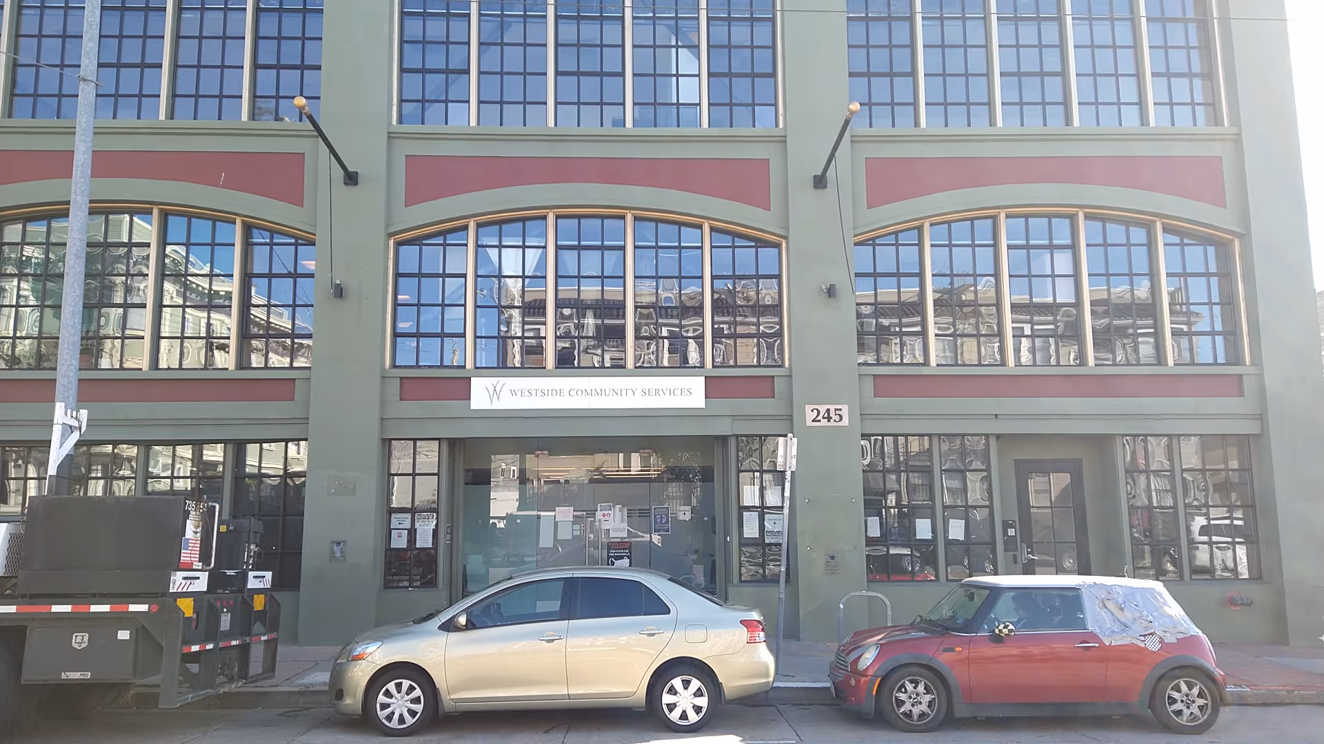 Front view of a green building with arched windows, sign 'Westside Community Services', and parked cars.