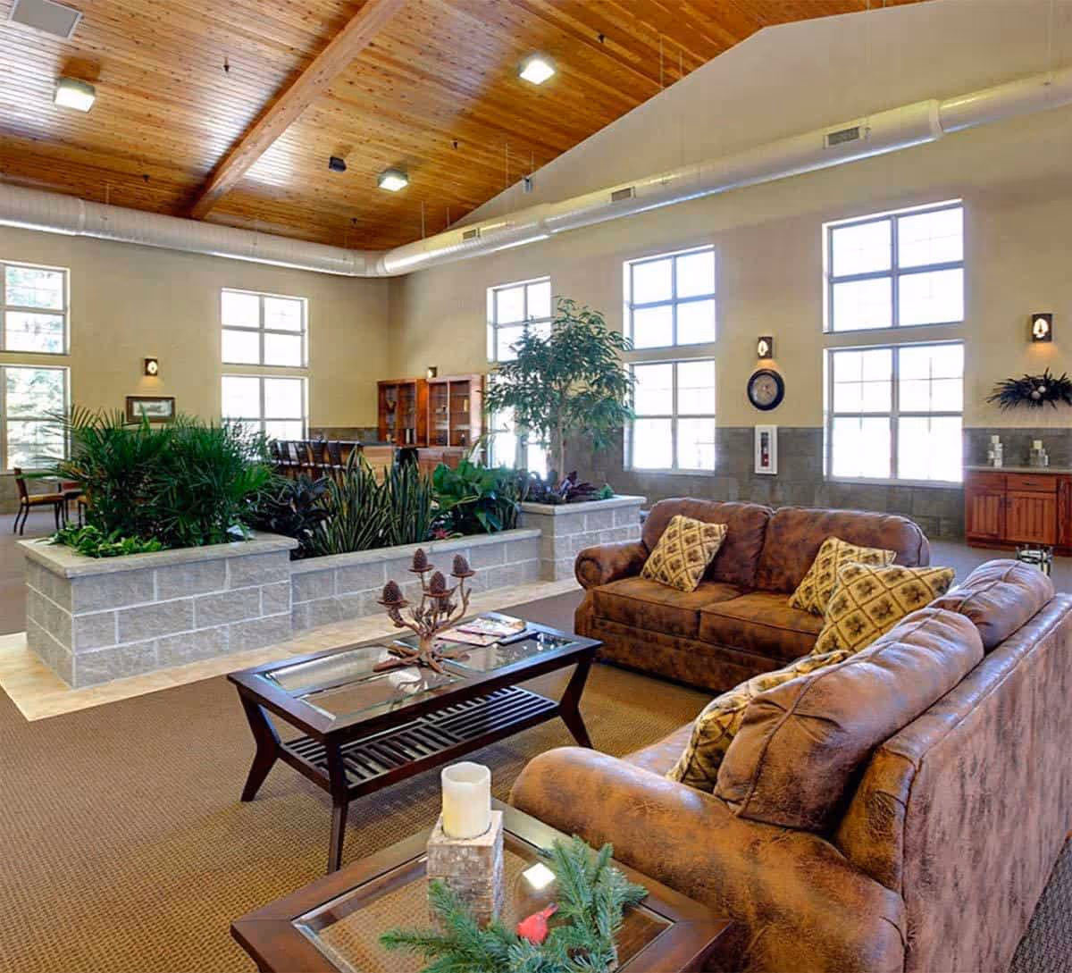 Elegant indoor lounge with brown sofas, glass coffee table, plants, and large windows.