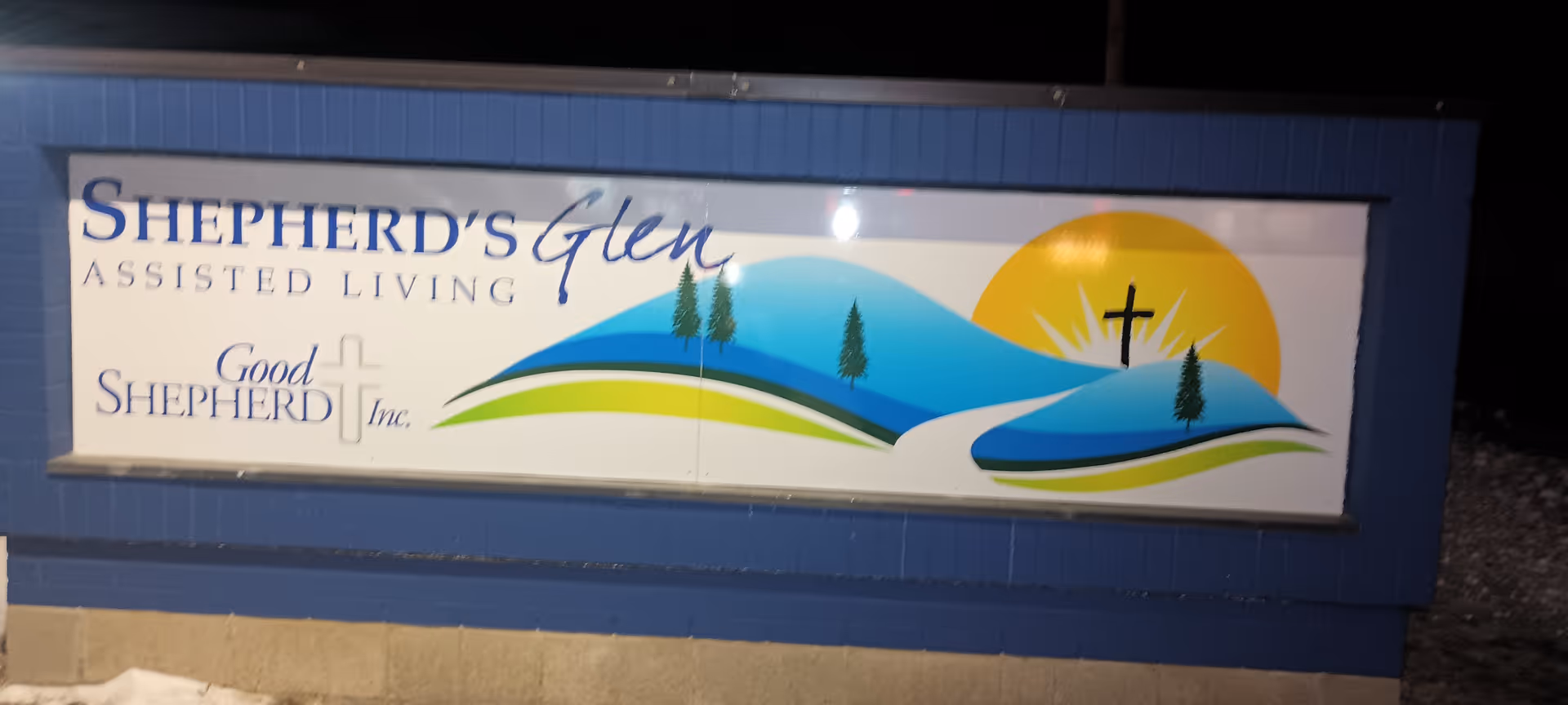 Blue building exterior with a large Shepherd's Glen Assisted Living sign and colorful hills art