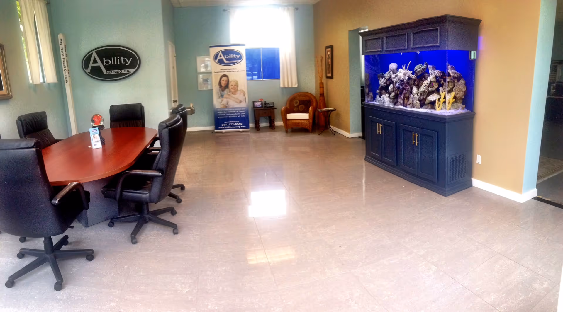 Office reception area with conference table, chairs, aquarium cabinet, and Ability Nursing signage.