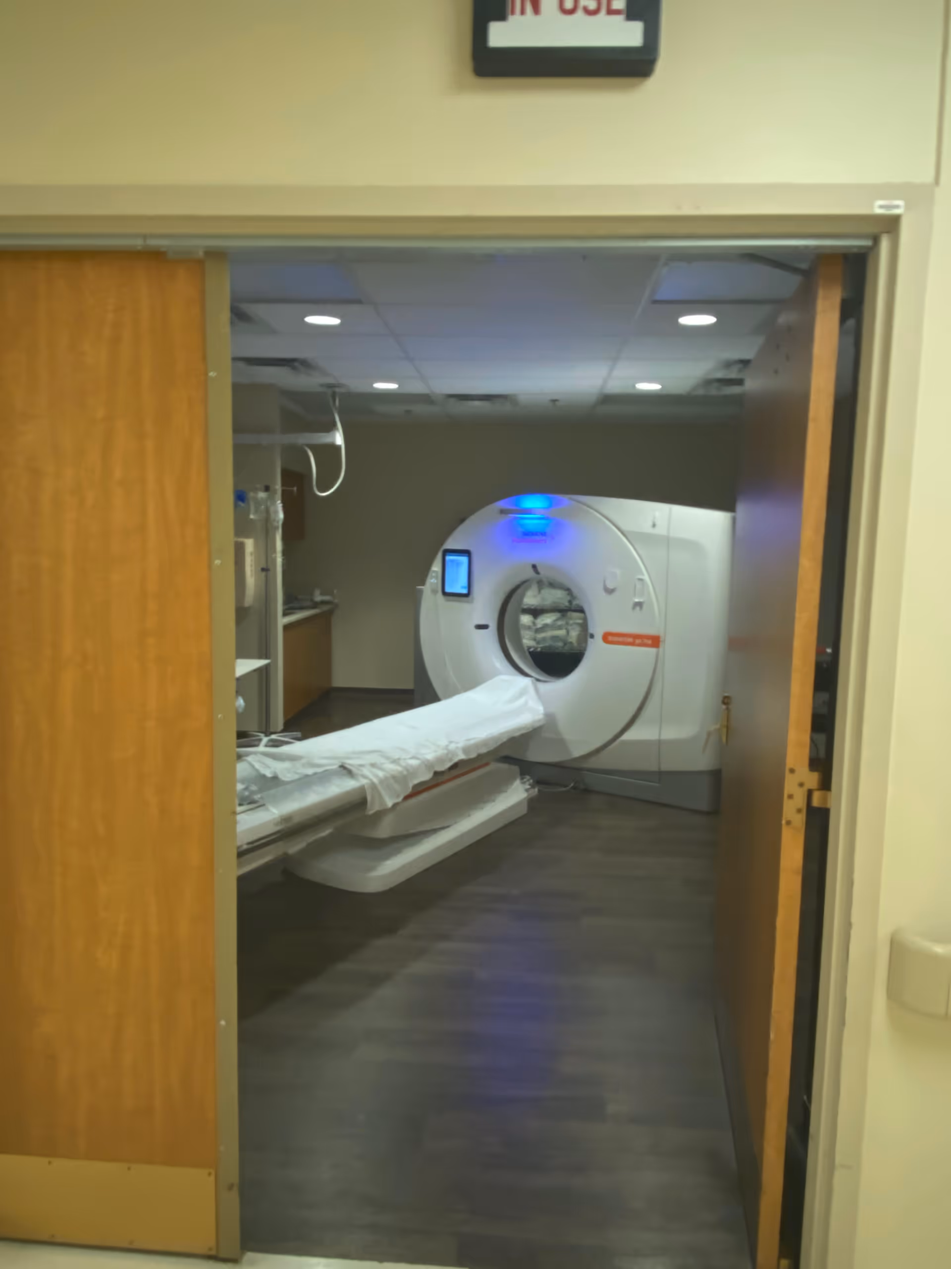 Hospital-style MRI room with a patient bed and a large MRI scanner.