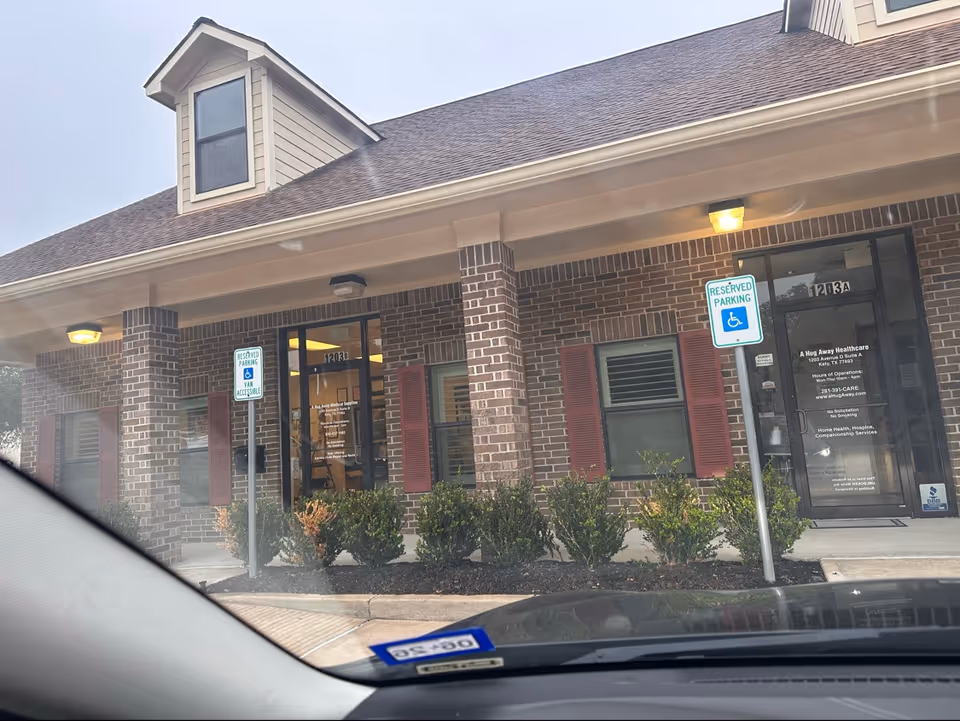 Front entrance of A Hug Away Healthcare, brick building with parking signs and shrubs.