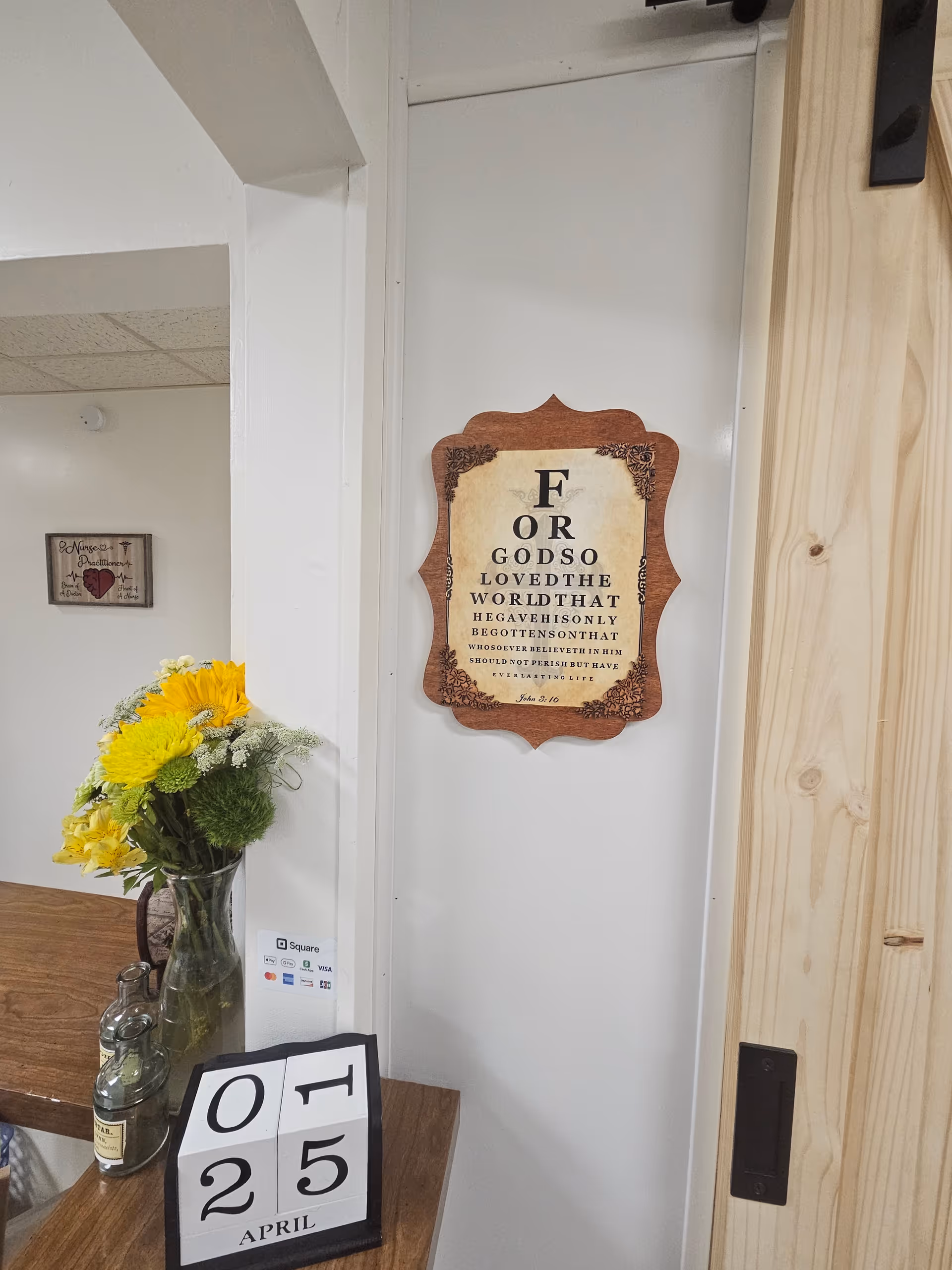 Indoor facility lobby area with a decorative sign, flowers, and a calendar on a table.