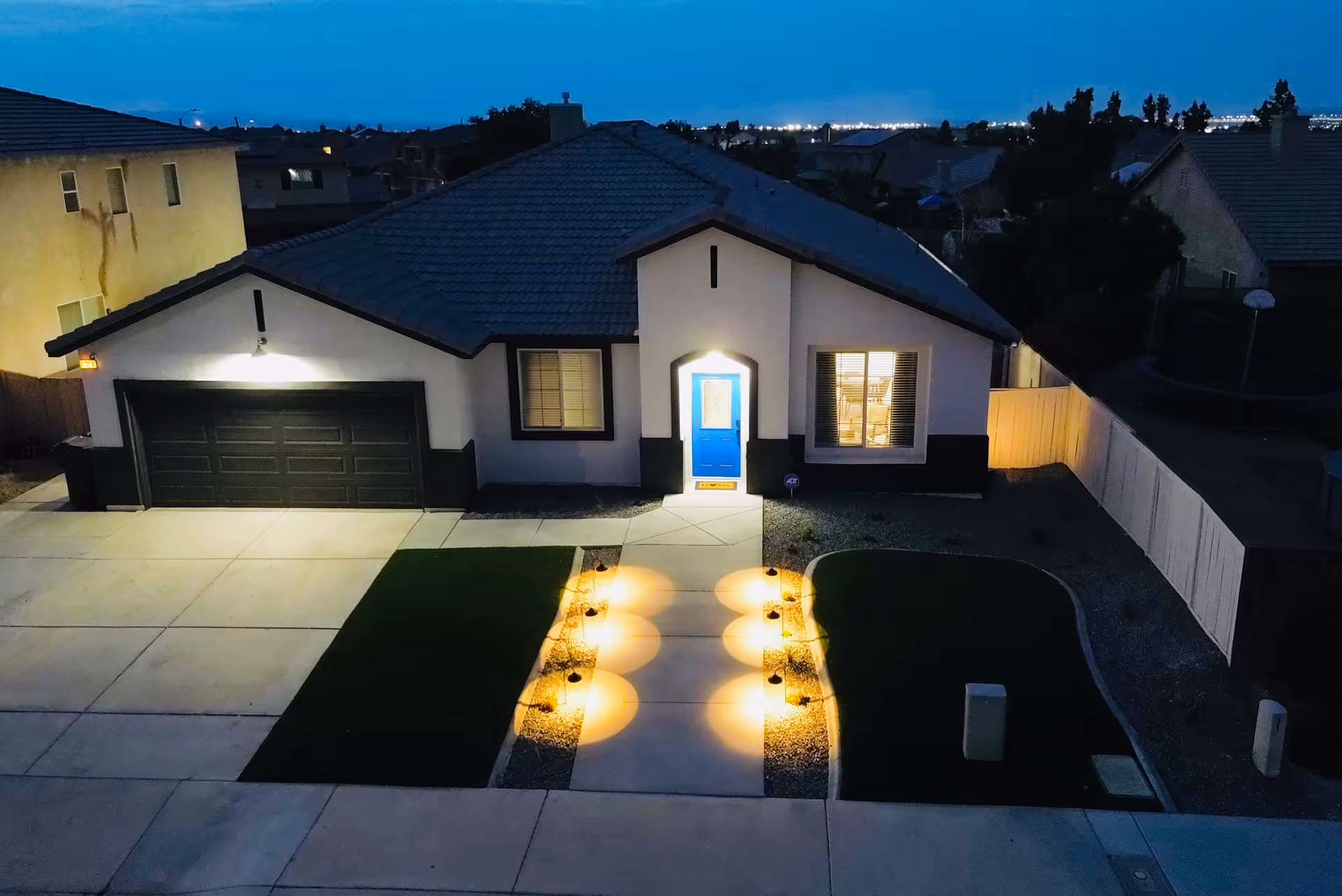 Front of a single-story home with a lit walkway and blue entry door.