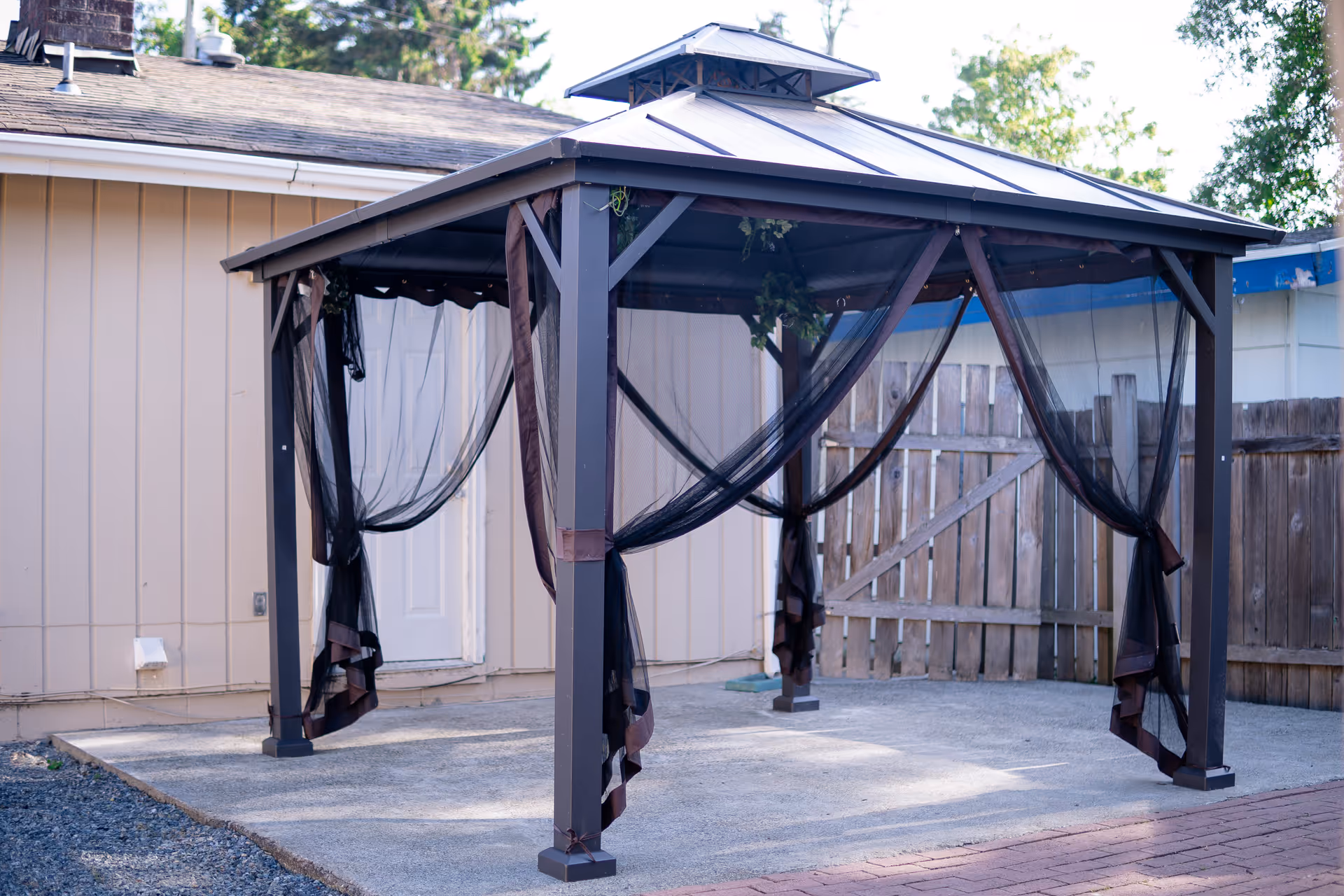 Outdoor gazebo with draped curtains in a paved backyard.