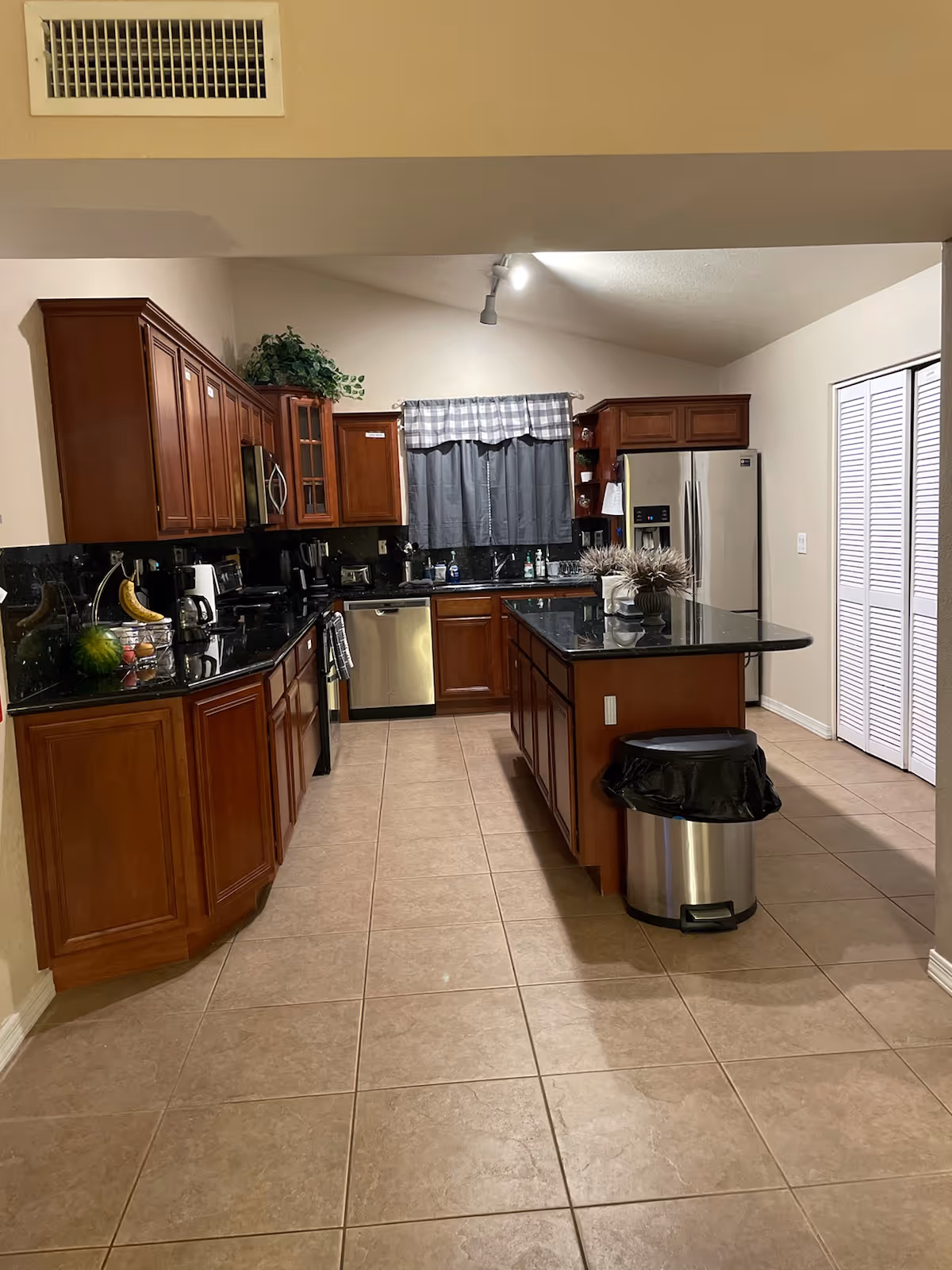 Spacious kitchen with dark granite countertops, wooden cabinets, island, and stainless steel appliances.
