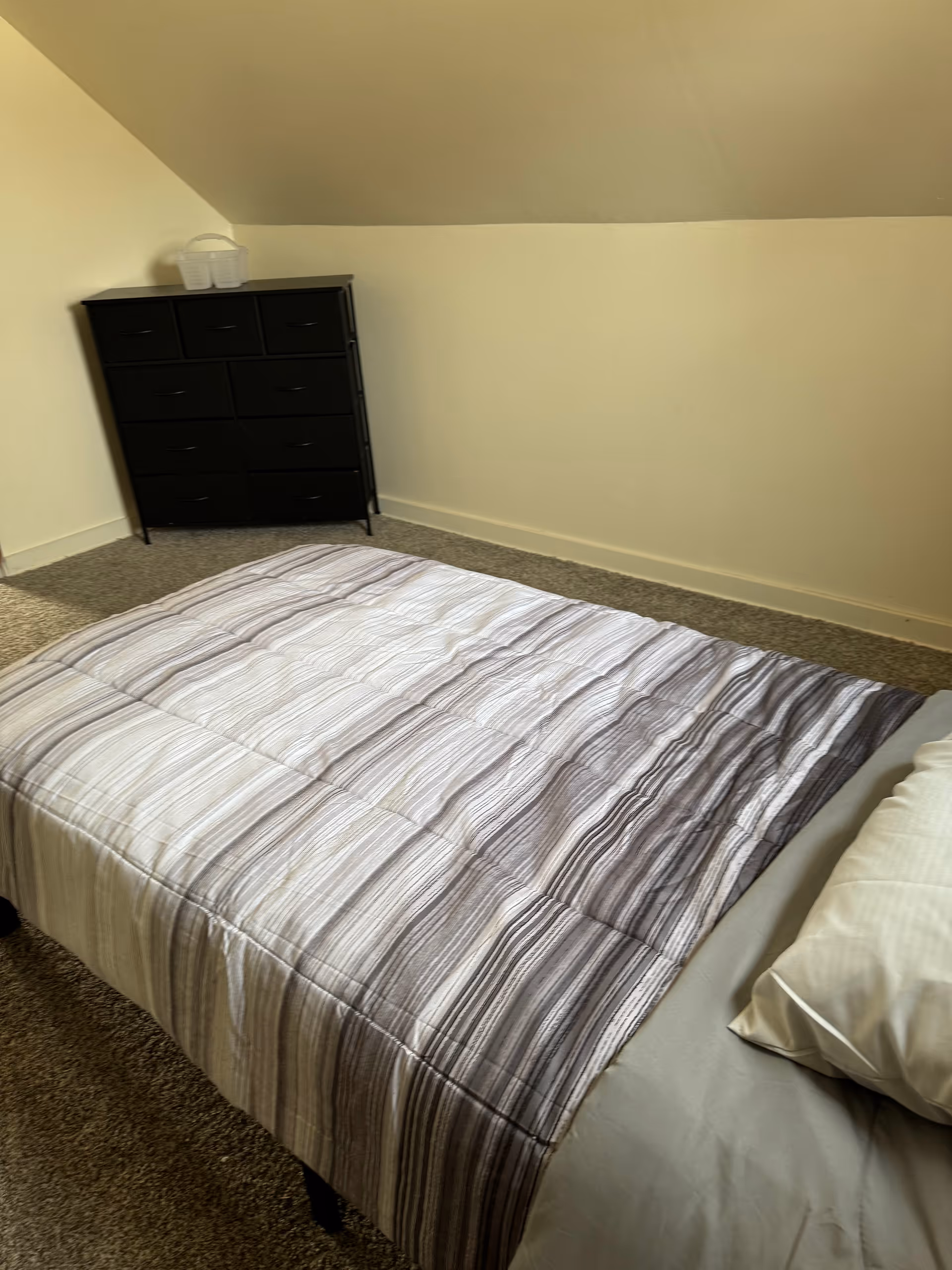 A bedroom in a senior living facility featuring a striped comforter, bed, and dresser.
