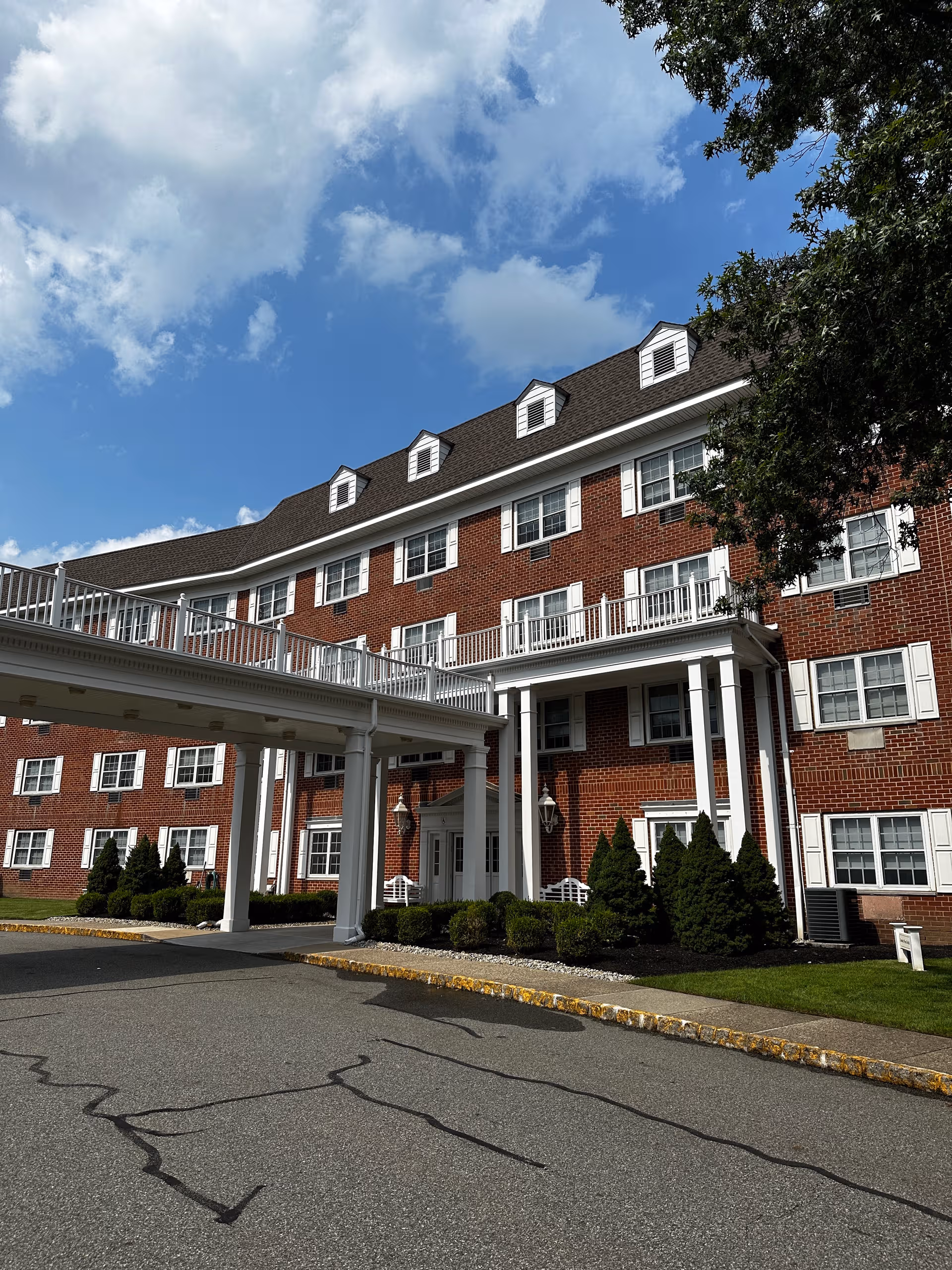 Brick senior living building with white columns and a covered front entrance under blue sky.