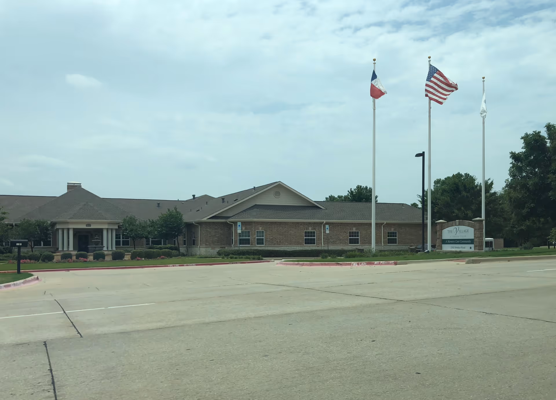 Front view of Eagle Ridge Alzheimer's Special Care Center: brick building, flags, sign, and parking.