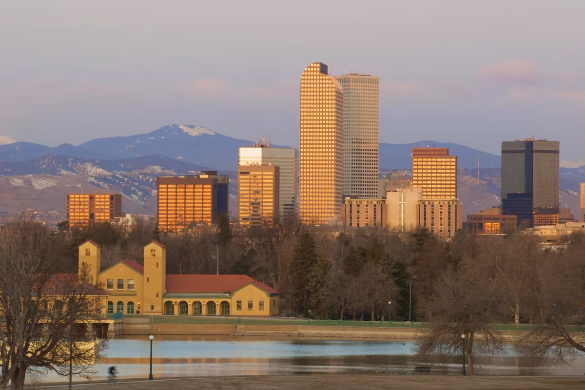 City skyline with river, mountains, and a yellow foreground building at sunset.