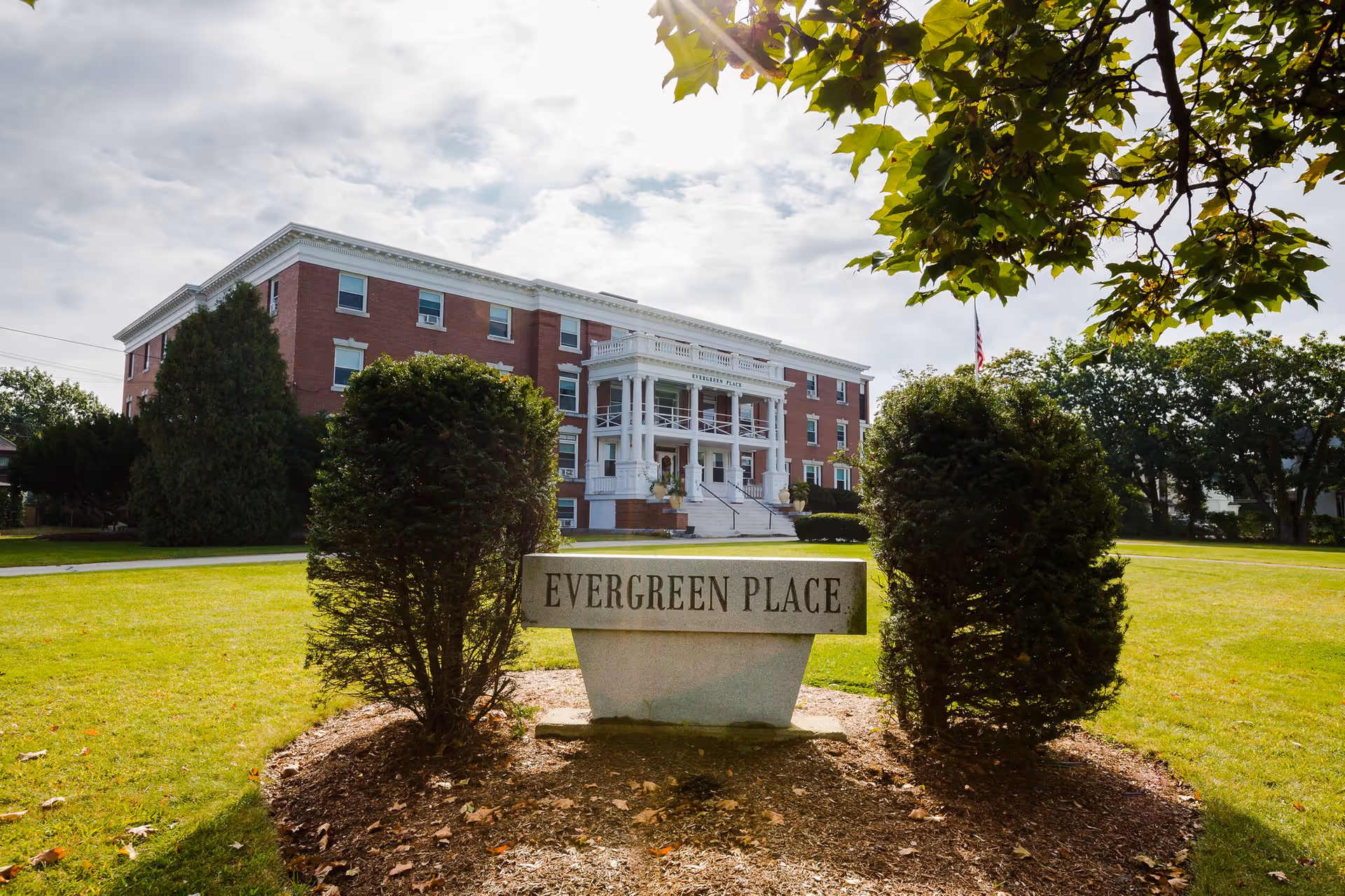 Brick building with columns and a sign reading Evergreen Place in the landscaped front yard.