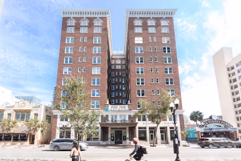 Tall brick twin-tower building with storefronts on ground floor and pedestrians on a city street.