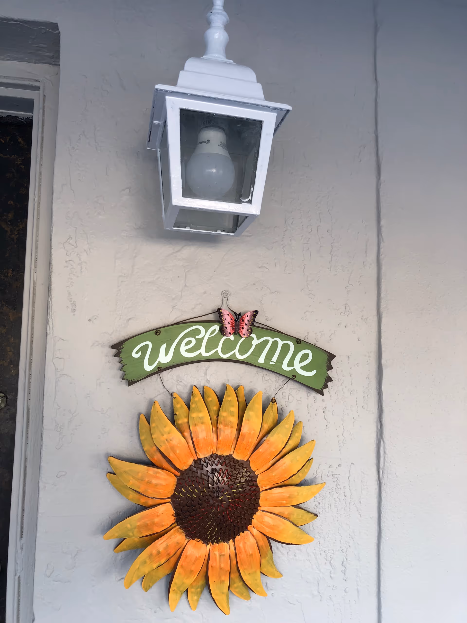 Outdoor wall displays a white lantern above a sunflower welcome sign