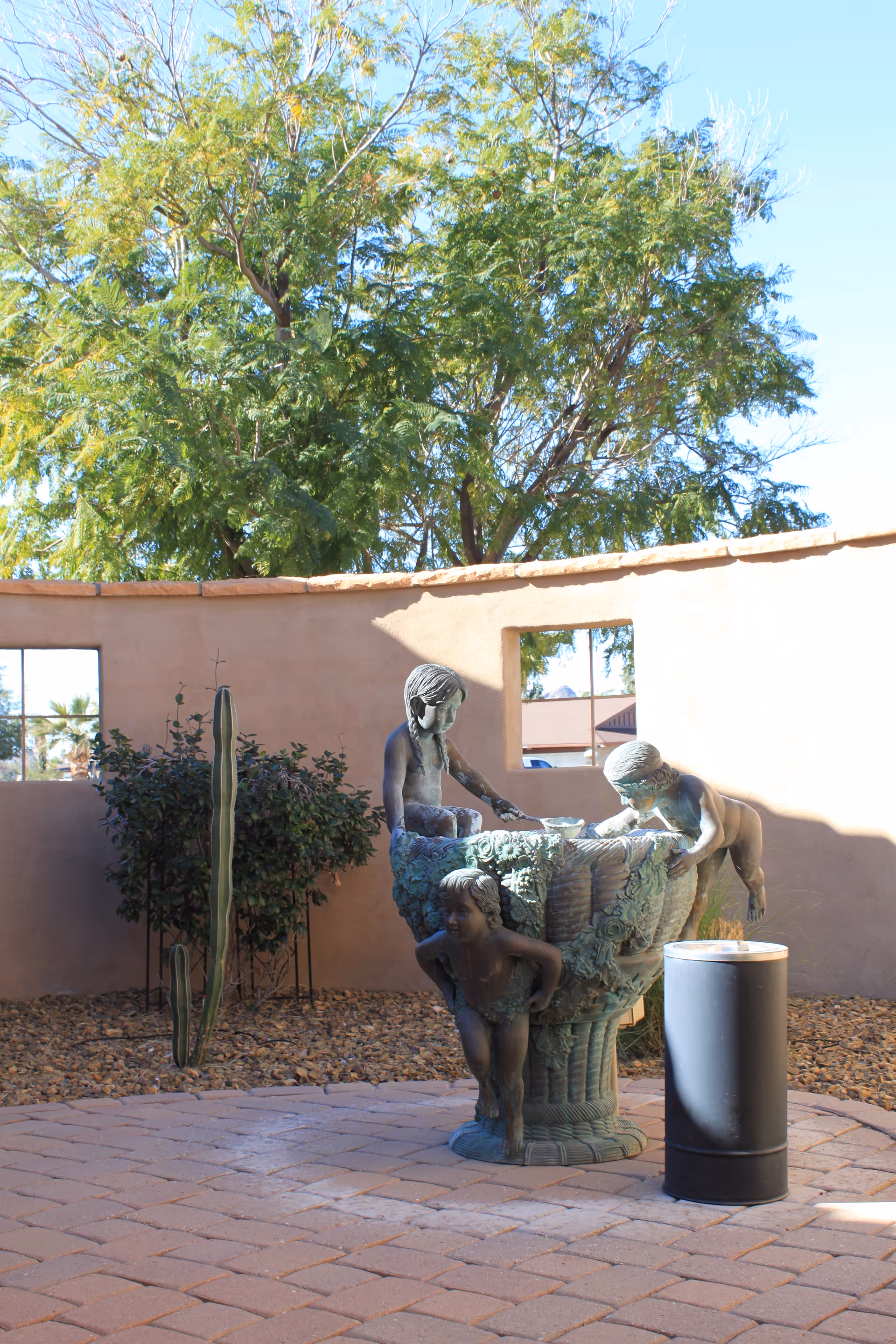 Outdoor courtyard with a sculptural fountain, cactus plants, and a peach-colored wall.