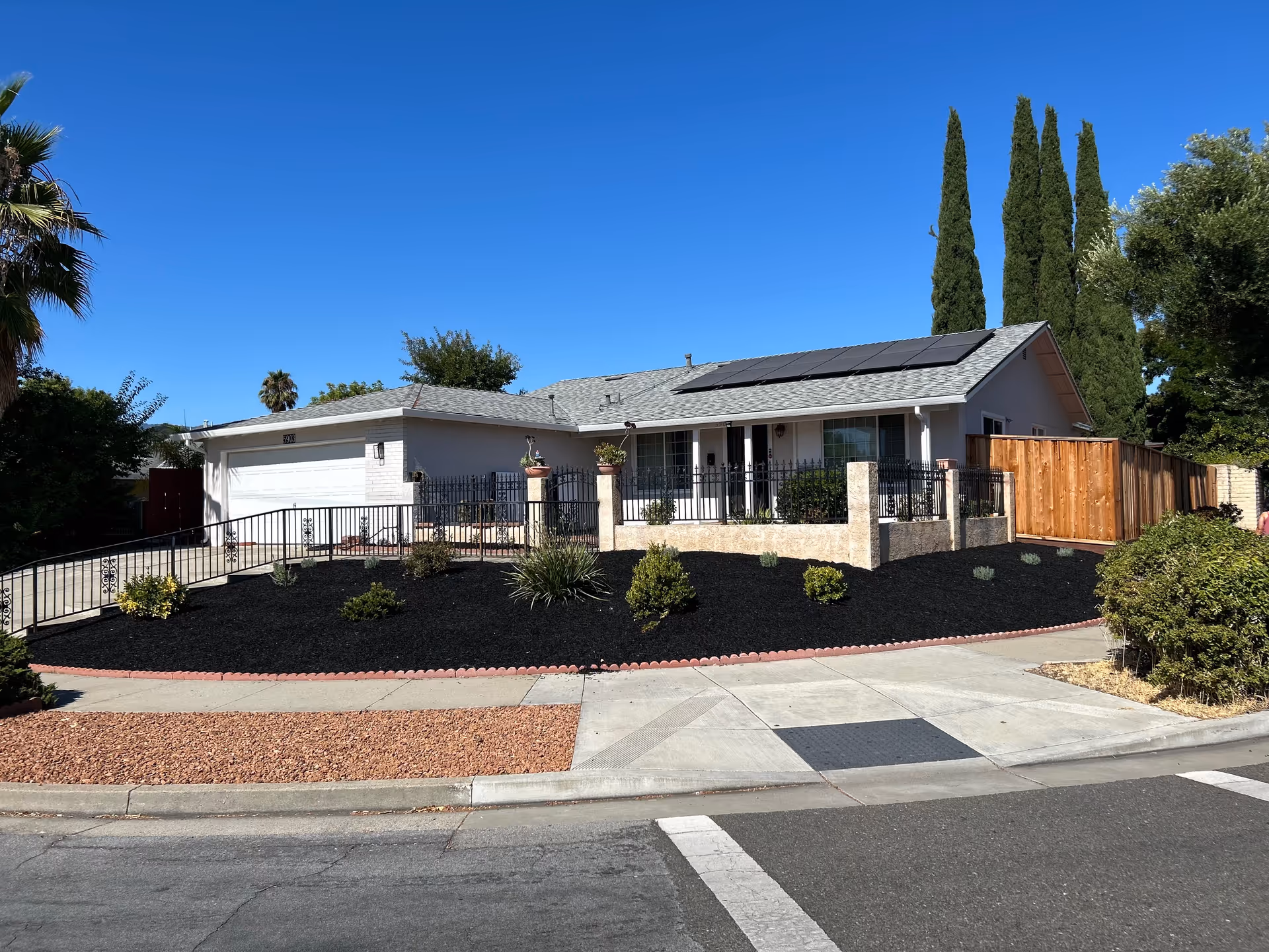 Single-story elderly care home exterior with a fenced front yard, dark mulch, and solar panels.