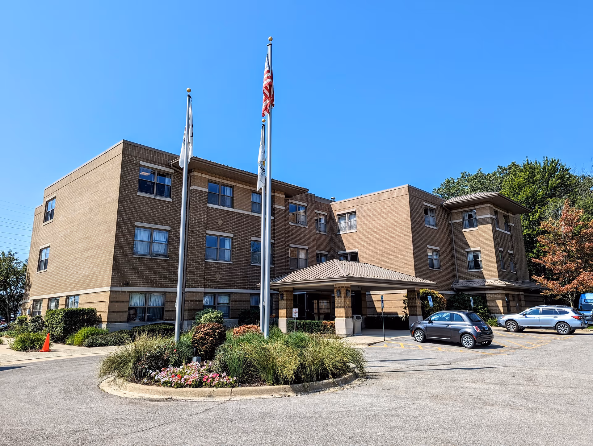 Brick senior care building with flags, entrance canopy, and cars in the parking lot.